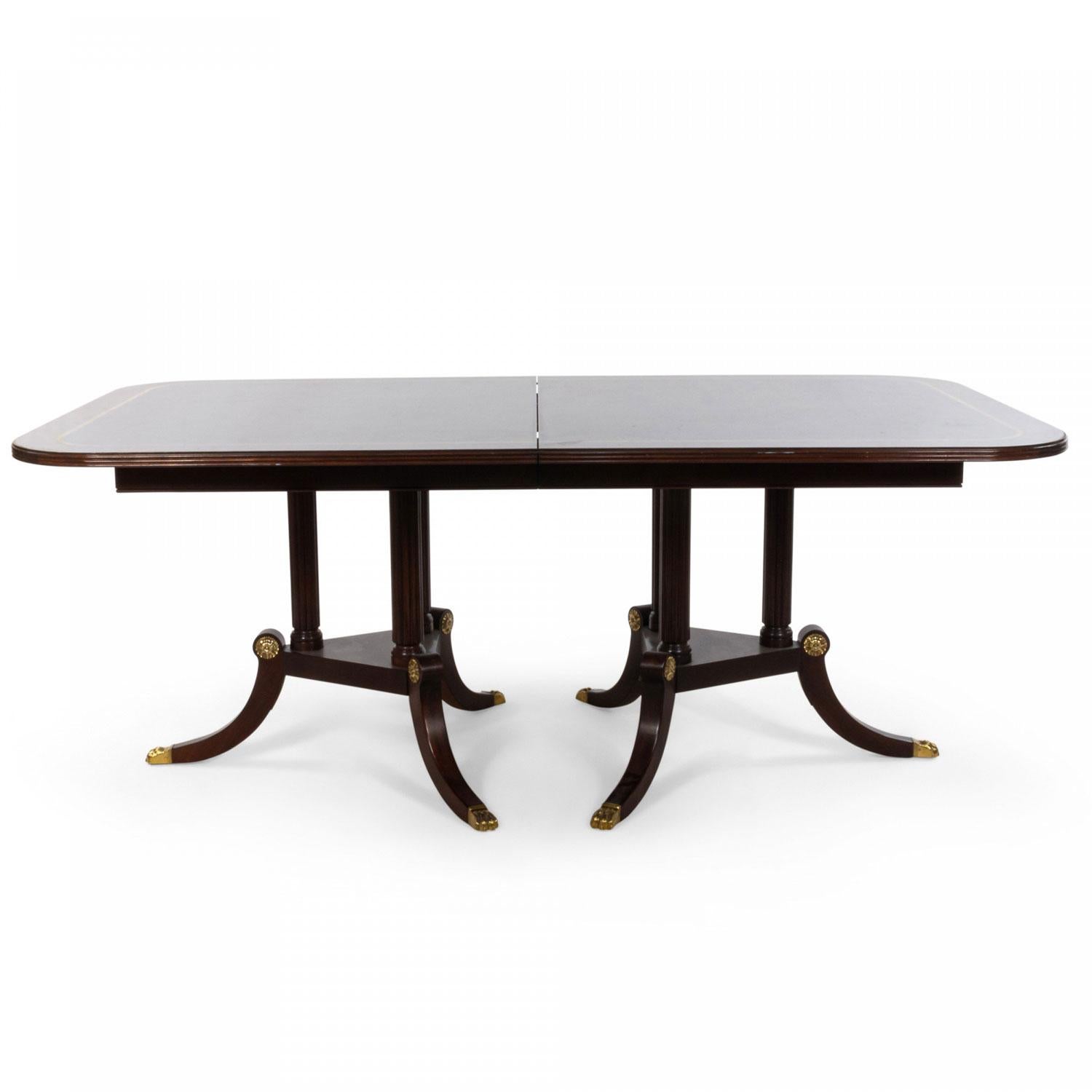 English Sheraton-style (20th century) mahogany dining table with satinwood inlaid perimeter supported by two tripartite reeded bases with saber legs ending in bronze gilt paw feet. (2 leaves - 16 inches each)

Large scratch on top of table, some