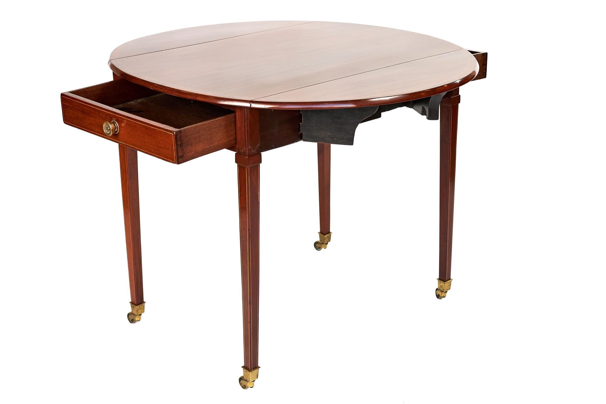 Table Pembroke en acajou marqueté de style Sheraton, vers les années 1930,
Plateau ovale avec bandes transversales et incrustation de lignes de buis,
Tiroirs à chaque extrémité avec doublures en chêne et queues d'aronde fines.
poignées en laiton
