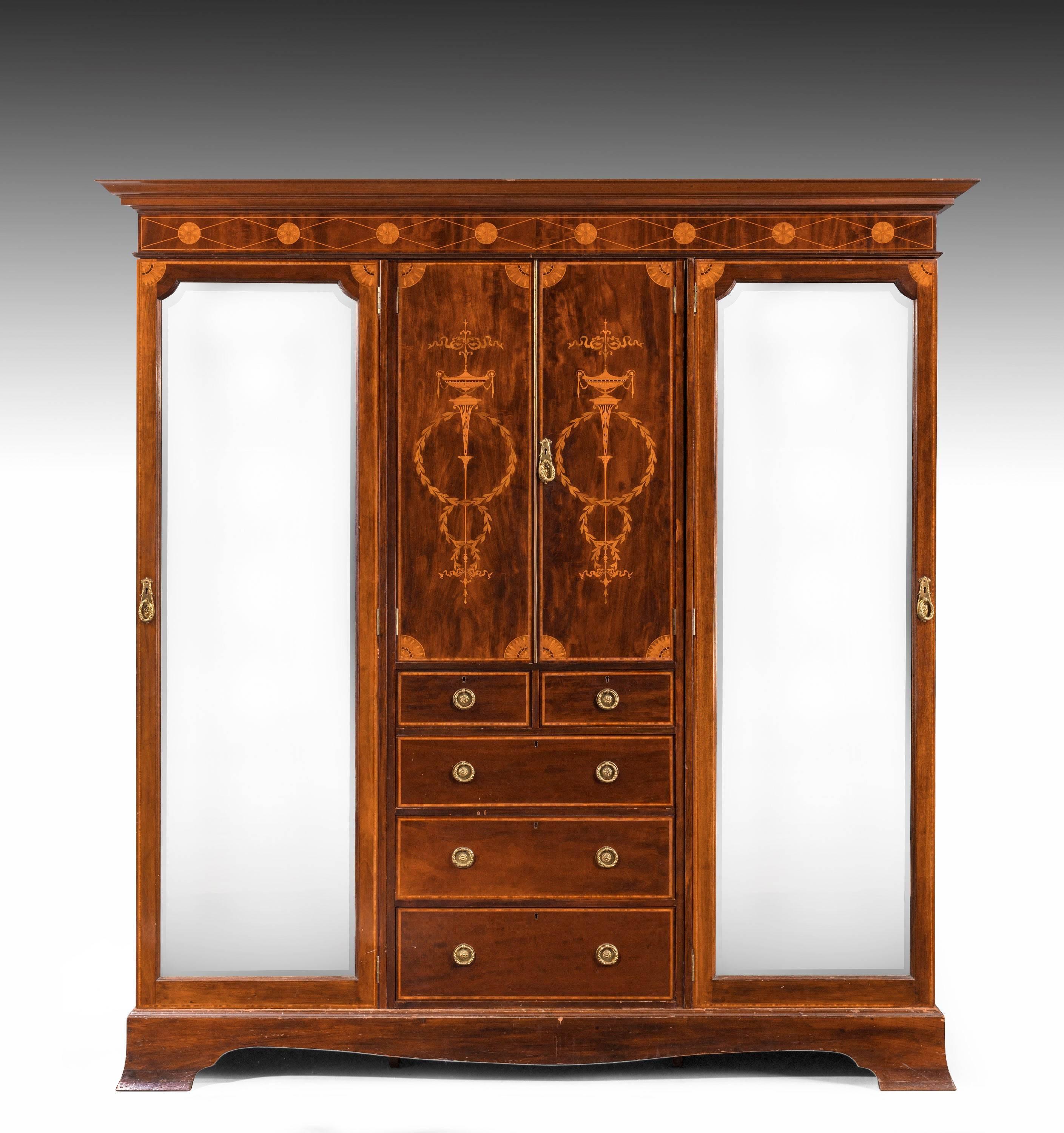 An attractive Sheraton style mahogany wardrobe. The doors fully mirrored with bevelled edges. The central part of the cupboard over five graduated drawers. Boxwood and satinwood inlay of marquetry and parquetry design.