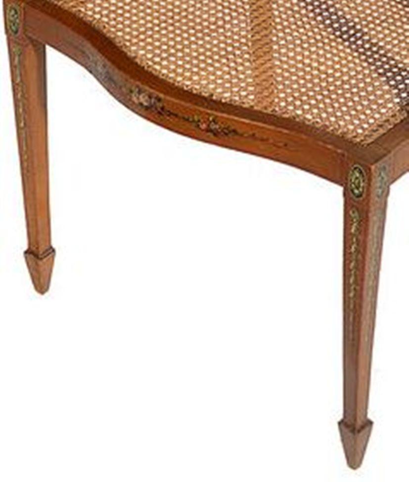 A  Sheraton style satinwood occasional chair with a caned seat and back and hand painted decoration throughout.

The whole supported on square tapering legs that end on spade feet to the front and outswept legs to the back.
 