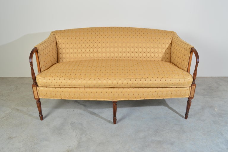 Sheraton-style settee with patterned silk-blend upholstery in a neutral cream color. Mahogany frame with curved arm fronts leading to fluted columns, maple inlay panels, turned front legs, and flared back legs. Late 20th century production.
 Very