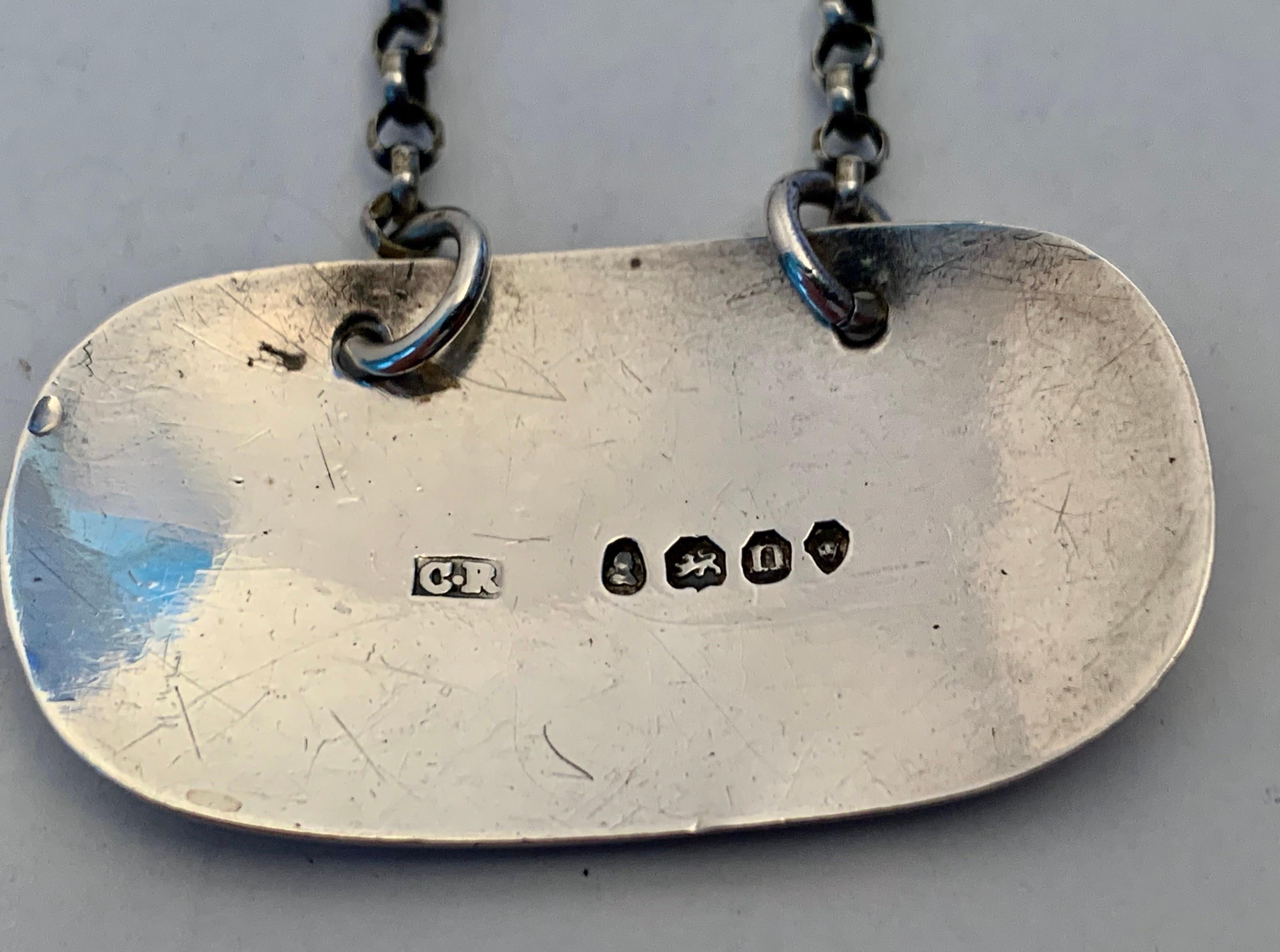 Etiqueta de decantador georgiano de plata de ley o ticket de botella si prefieres el estilo inglés, hecha a mano por el platero Charles Rawlings en Londres, en 1828, durante el periodo de Jorge IV.  Lleva la marca C.R. en una cartela rectangular.   