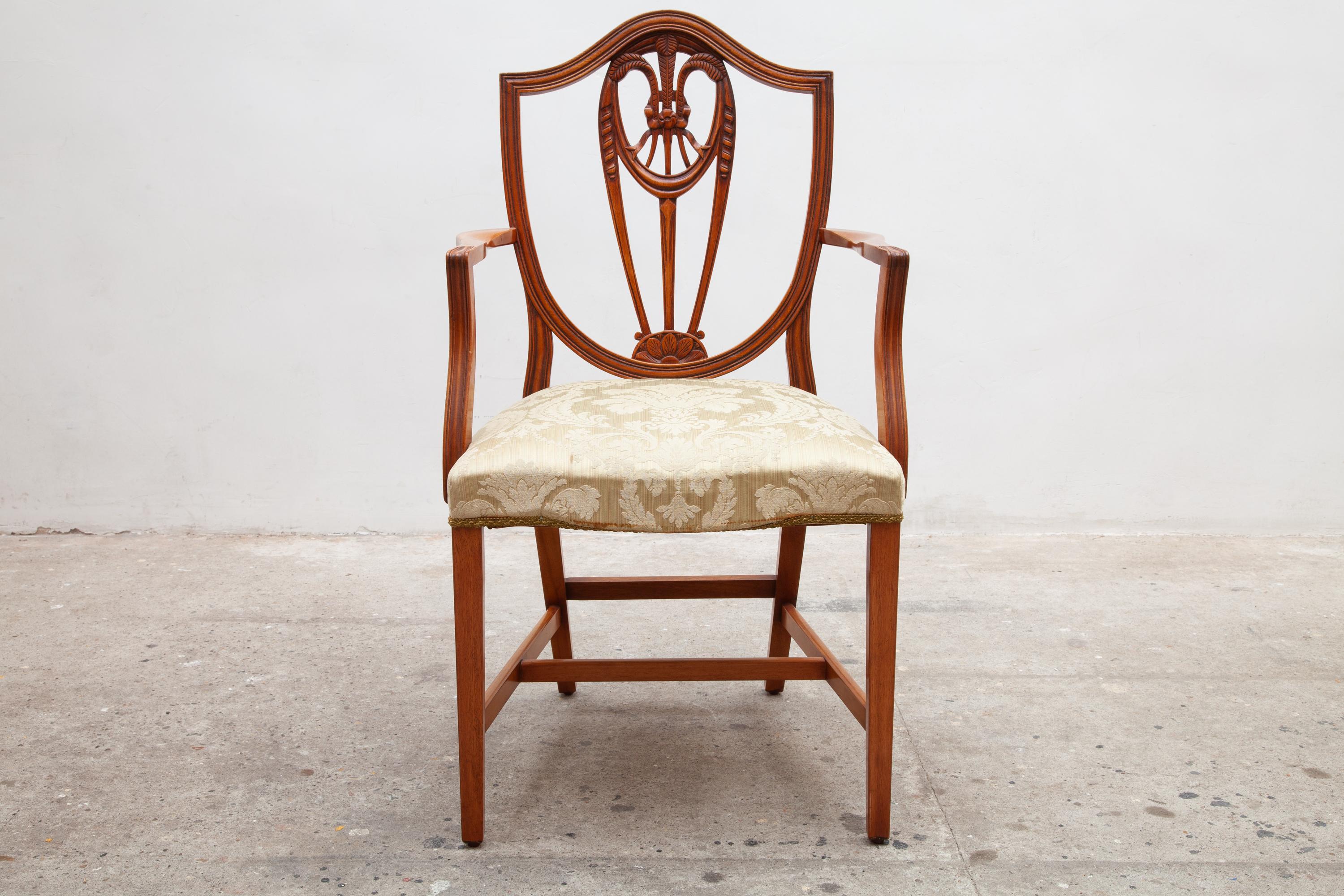 Cet ensemble de deux chaises en noyer massif à un seul bras présente un dossier en bouclier de style Hepplewhite avec des motifs de gerbes de blé sculptés au centre. Ils sont dotés de sièges rembourrés et reposent sur des pieds avant en forme de