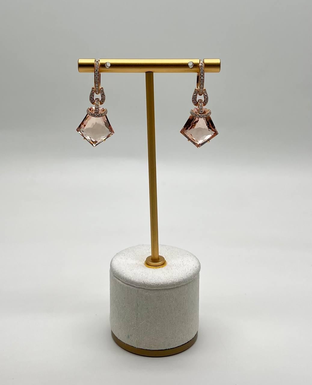 These exquisite earrings feature a modern design with geometric peach pink Morganites in fancy shield kite shapes. The earrings are adorned with sparkling accents along the hoops and connectors, adding a touch of sophistication. Crafted with