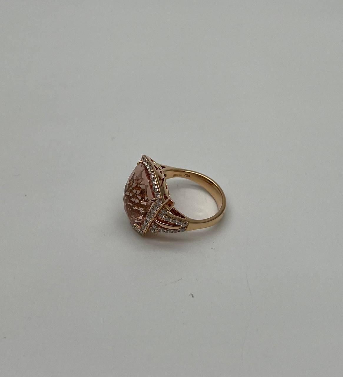 This exquisite ring is crafted with a stunning central peach-colored morganite cut in a shield kite shape, surrounded by a halo of sparkling clear diamonds. The setting features intricate detailing, enhancing the brilliance of the central gem. The