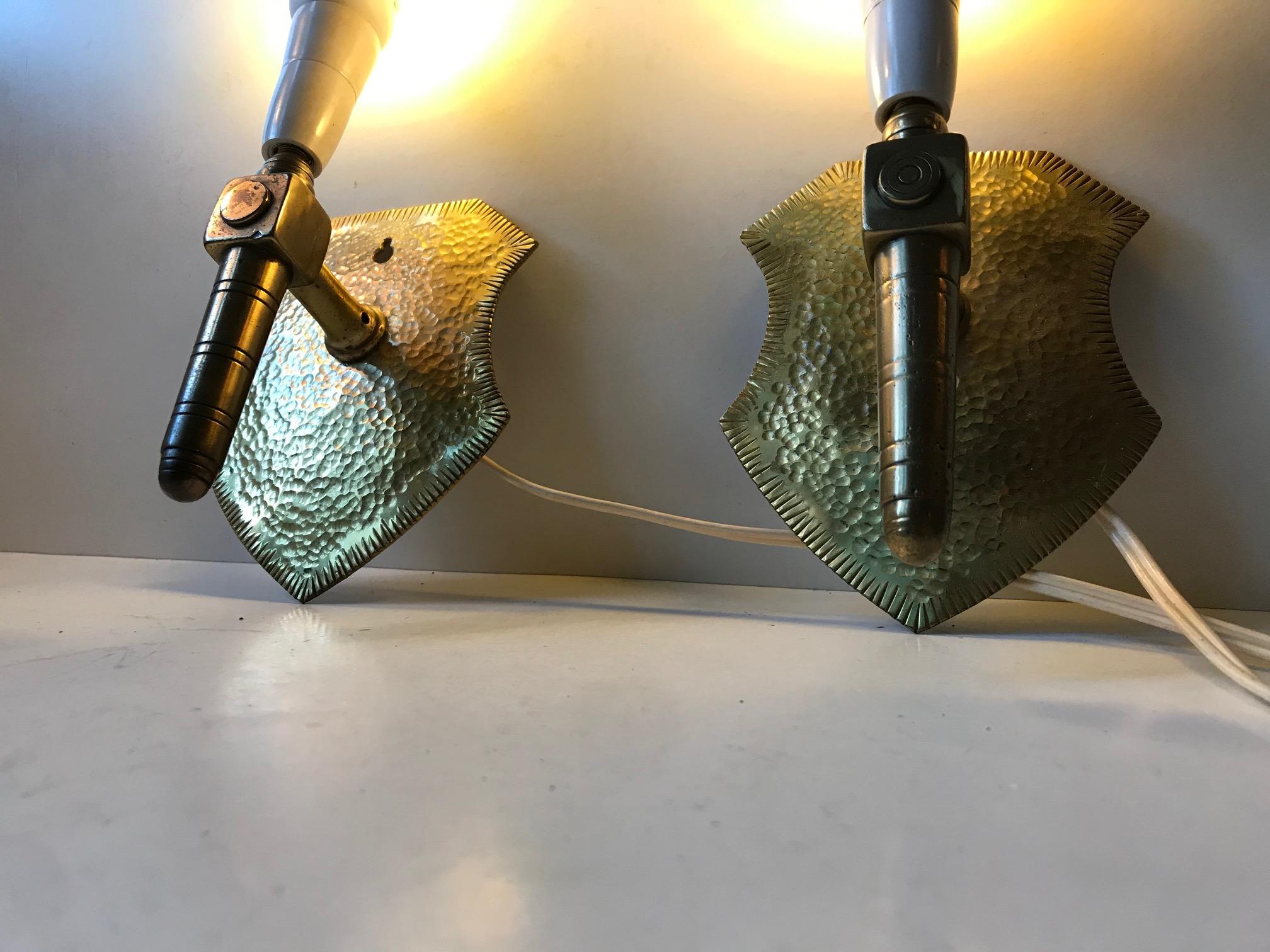 Unusual pair of wall lights made entirely from brass. The wall mounts are shaped as shields and the overall design resembles Gothic Revival. It is rare to see such 'masculinity' displayed in sconces. These lights comes as a pair but without shades.