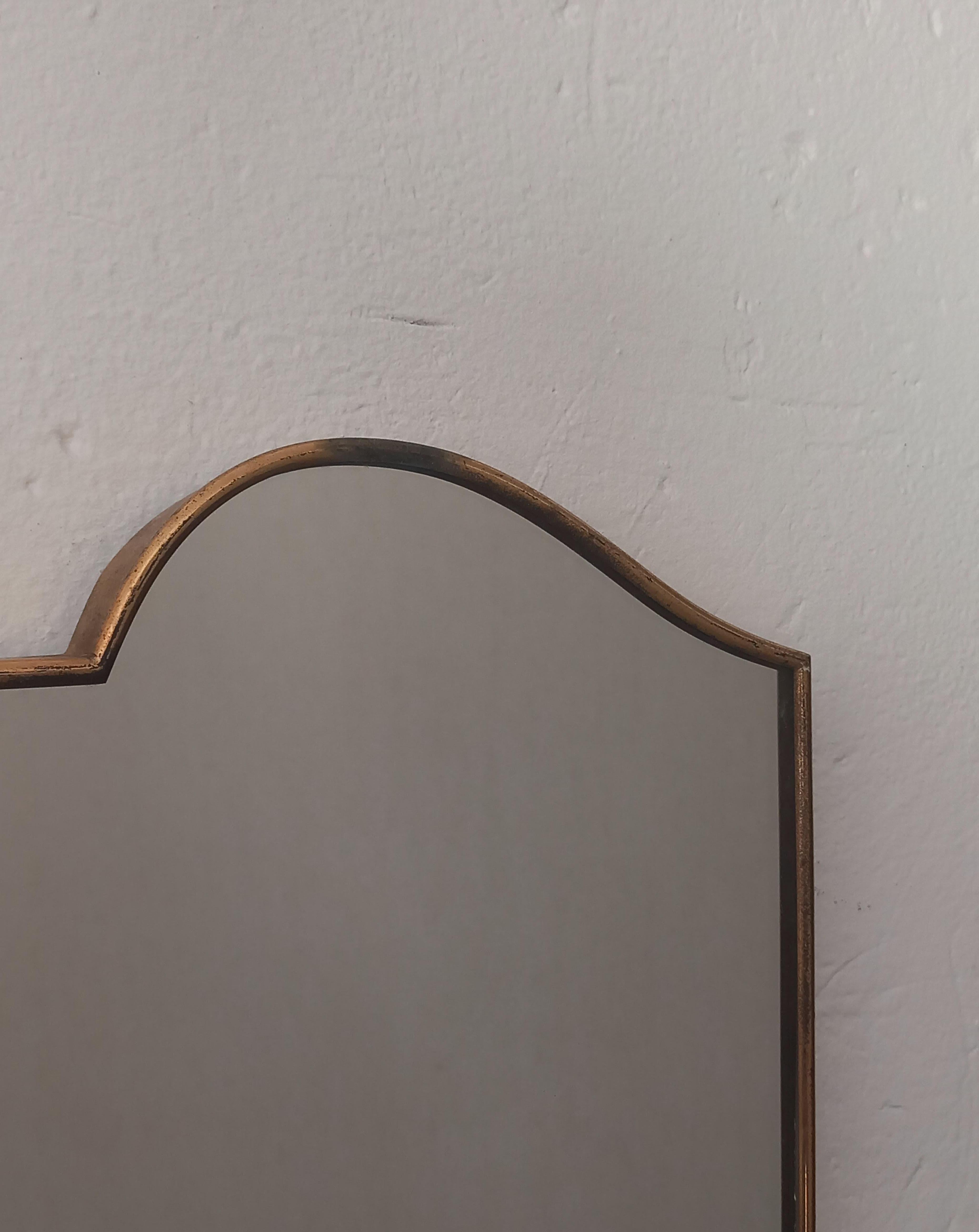 Add timeless charm to your space with this vintage mirror from the 1950s, expertly crafted with a distinctive shield shape and a refined brass frame that exudes elegance. The frame shows a beautiful patina and signs of wear, enhancing its authentic