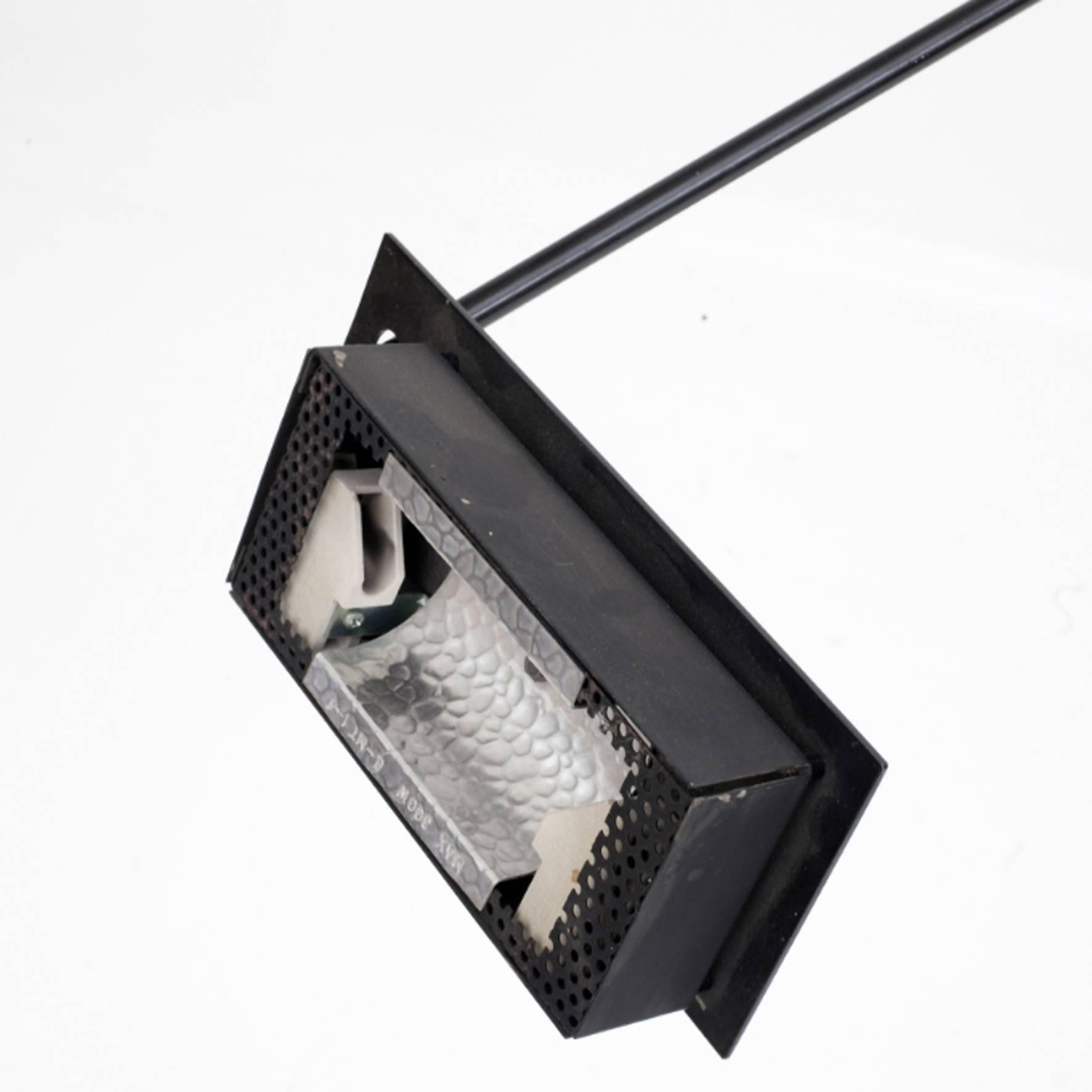 A black metal floor lamp. The rectangular shape reflector on an articulated arm terminated by a counterpoise supported by a double stem on a square base.
Original edition by Stilnovo.
 