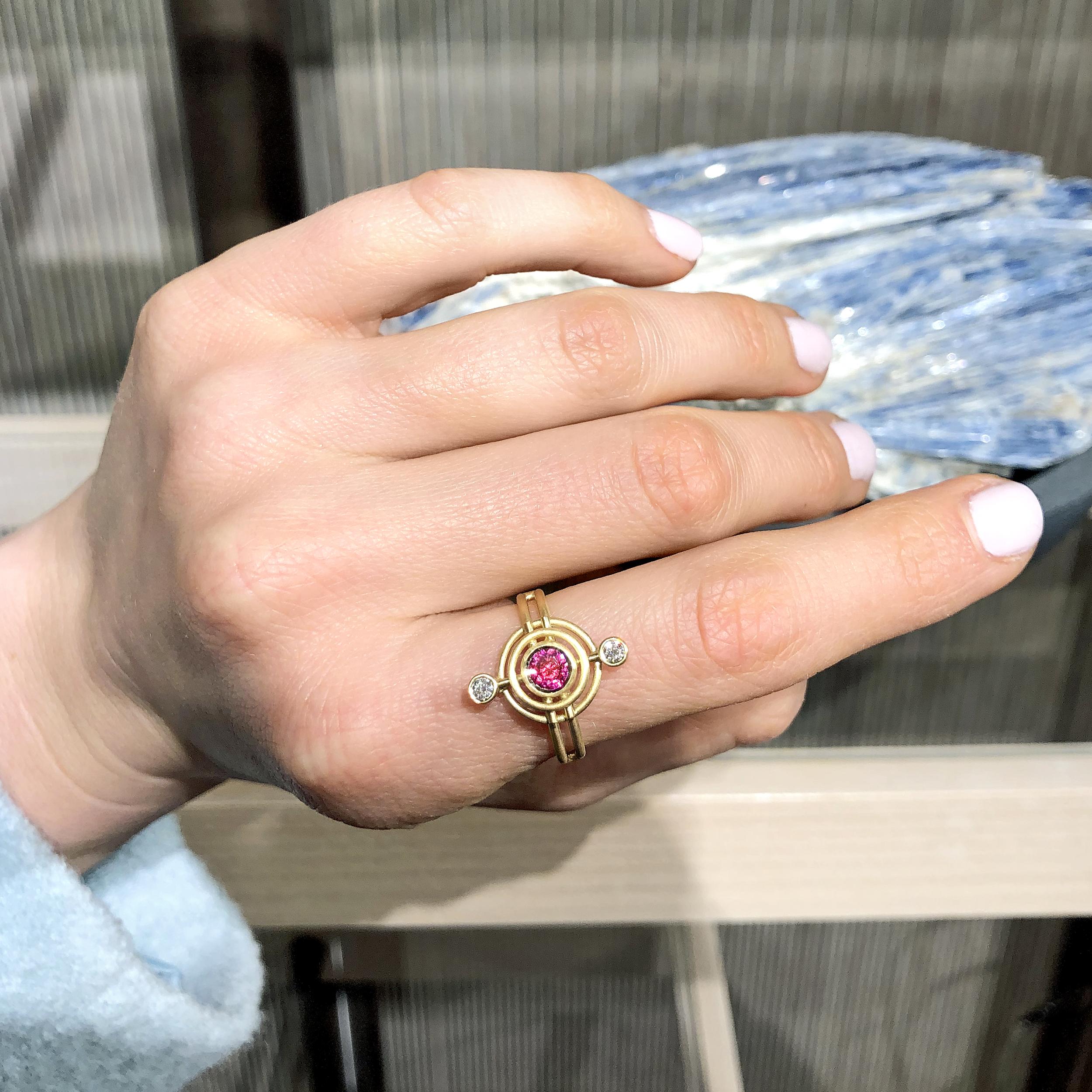 One of a Kind Double Circle Galaxy Ring handcrafted in London by jewelry maker Shimell and Madden in intricately-textured 18k yellow gold featuring a fiery and vibrant round faceted brilliant-cut 0.59 carat deep pink sapphire complemented by two