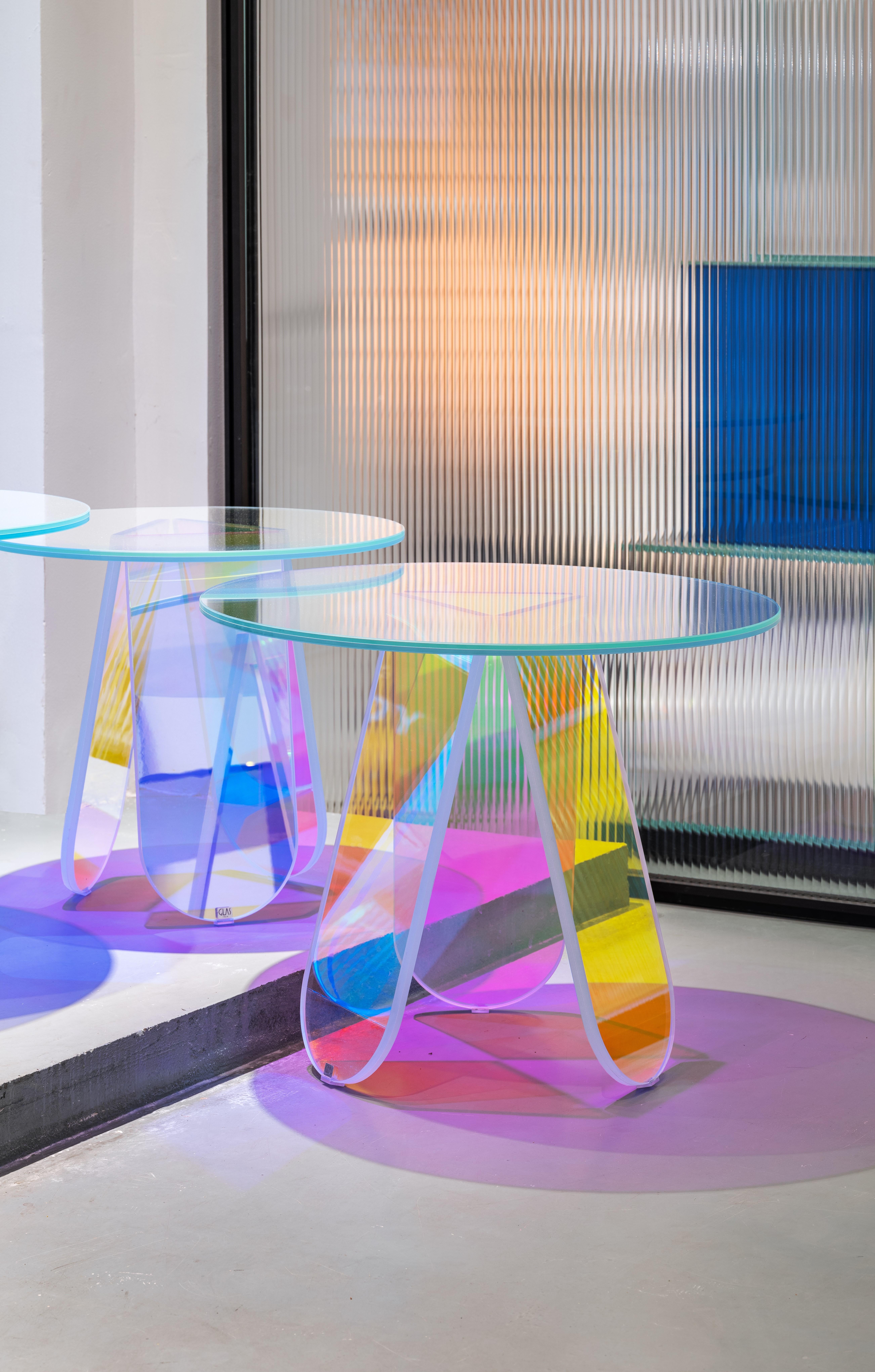 Shimmer rounded table is shown here with laminated and glued glass, and in the medium size of the two rounded tables. The collection consists of low tables, low tables and consoles in laminated and glued glass, characterized by a special iridescent
