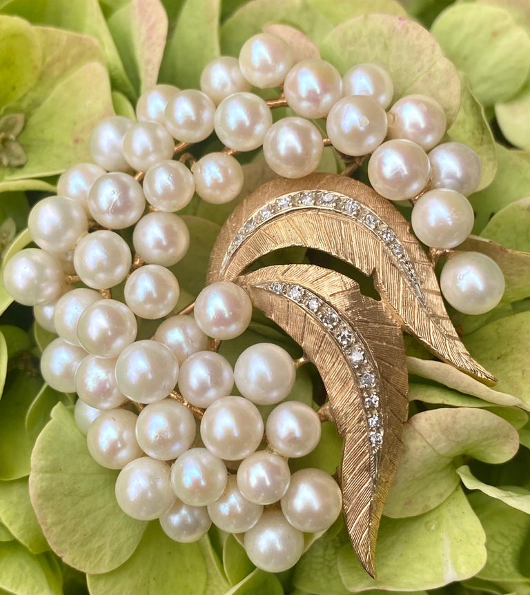 Very flowing, three dimensional, cluster of lustrous ivory tone pearls with leaves design vintage estate brooch pin is depicted in 14 karat yellow gold. It is accented with rows of white diamonds down the middle of each leaf and features beautiful
