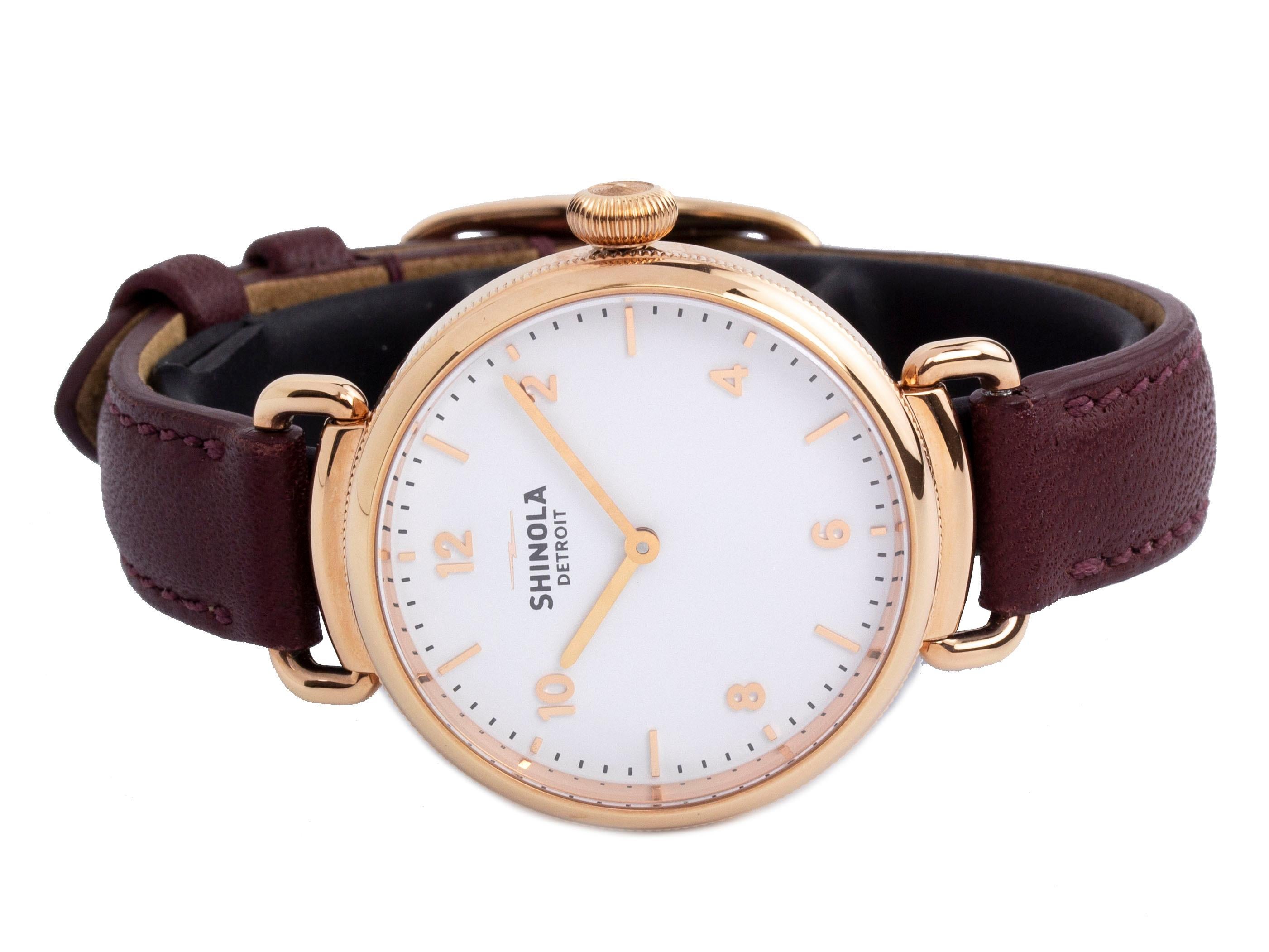 Rose gold-tone steel Shinola The Canfield quartz watch with a 32mm case, white dial, and burgundy leather strap with tang buckle. Features include hours and minutes. It comes with a Generic Gift Box and 2 Year Store