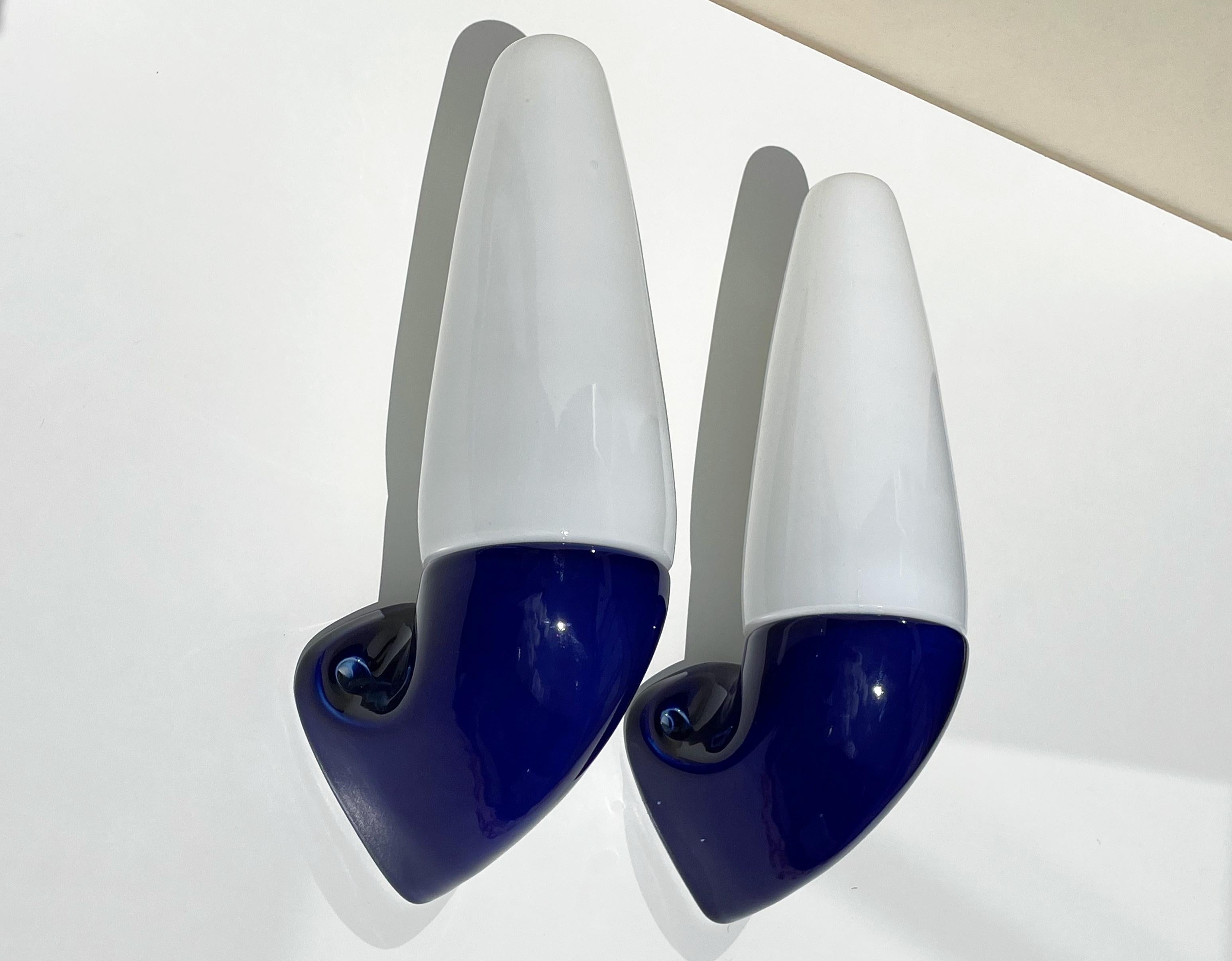 Set of two Swedish midcentury modern vintage wall sconces designed by artistic director for Ifö, Stig Carlsson (1932-2008) in the early 1960s. Shiny cobalt blue glazed mount with cone shaped white opaline glass top. Original porcelain fitting for