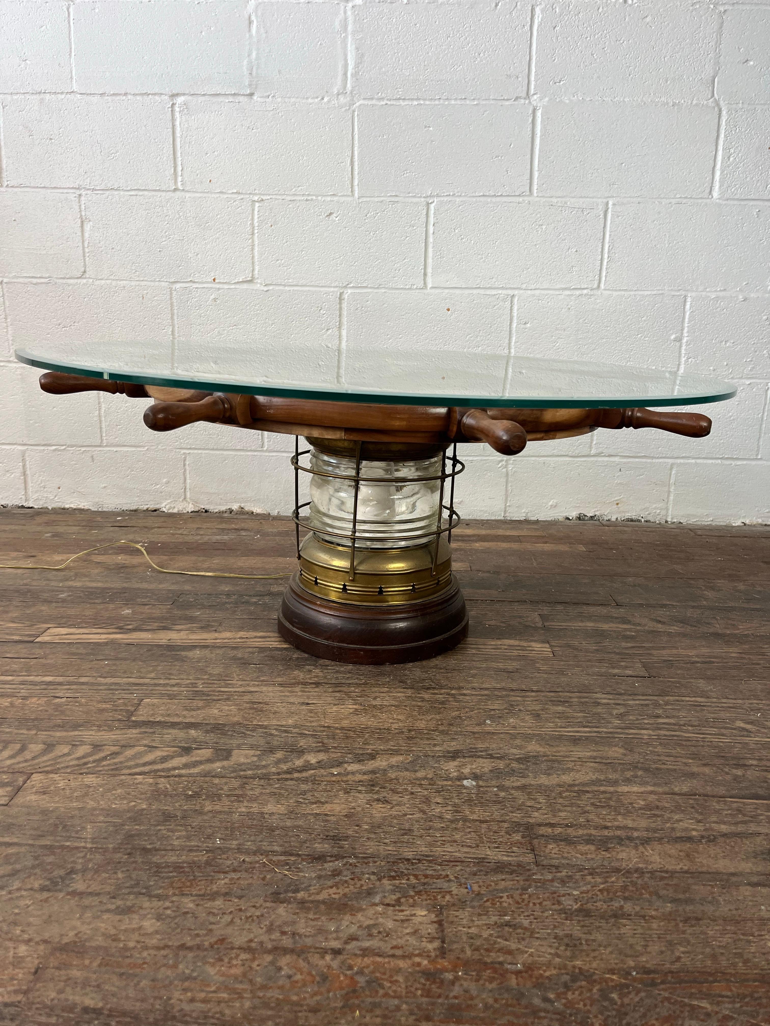Estupenda mesa de centro con forma de rueda de barco y base iluminada. Farol de latón y tapa central de latón. Parte superior con borde biselado de 38