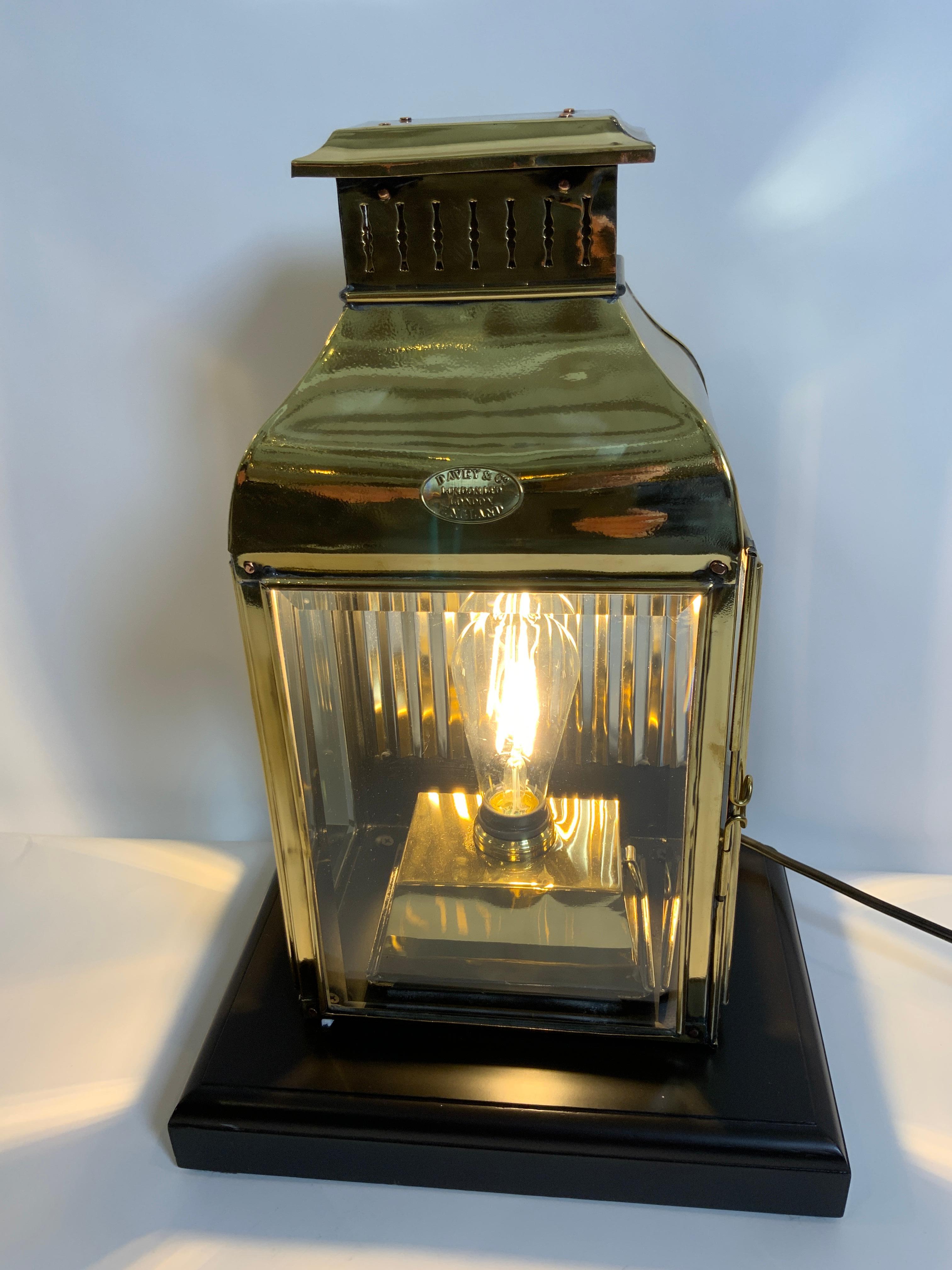 Early twentieth century highly polished and lacquered ships cabin lantern with three beveled glass panels, back reflector and hinged door. Mounted to a varnished wood base. With makers badge 