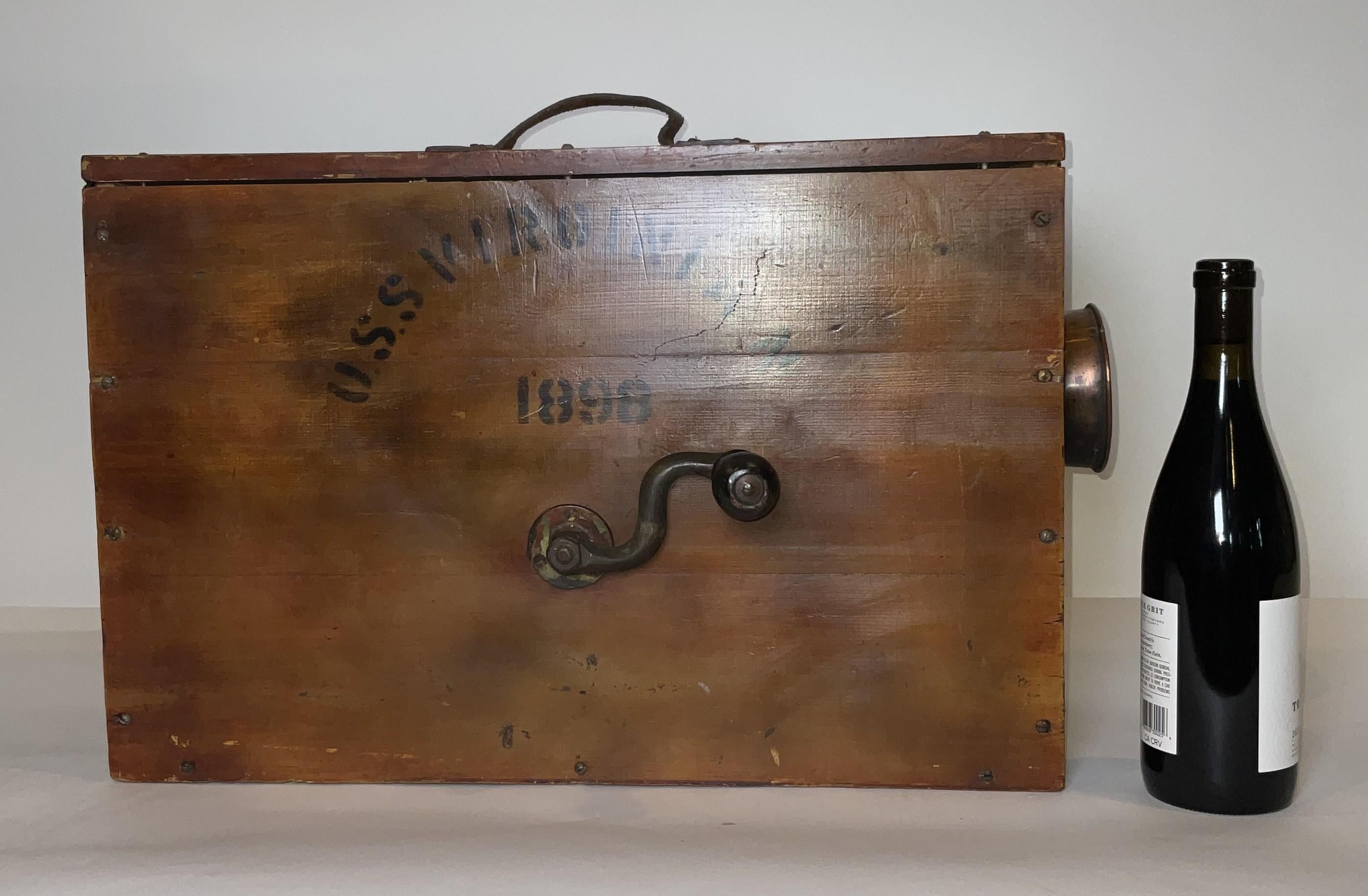 Crank handle bellows foghorn in a wood box with leather carry handle and copper trumpet. Lettering on the side reads 