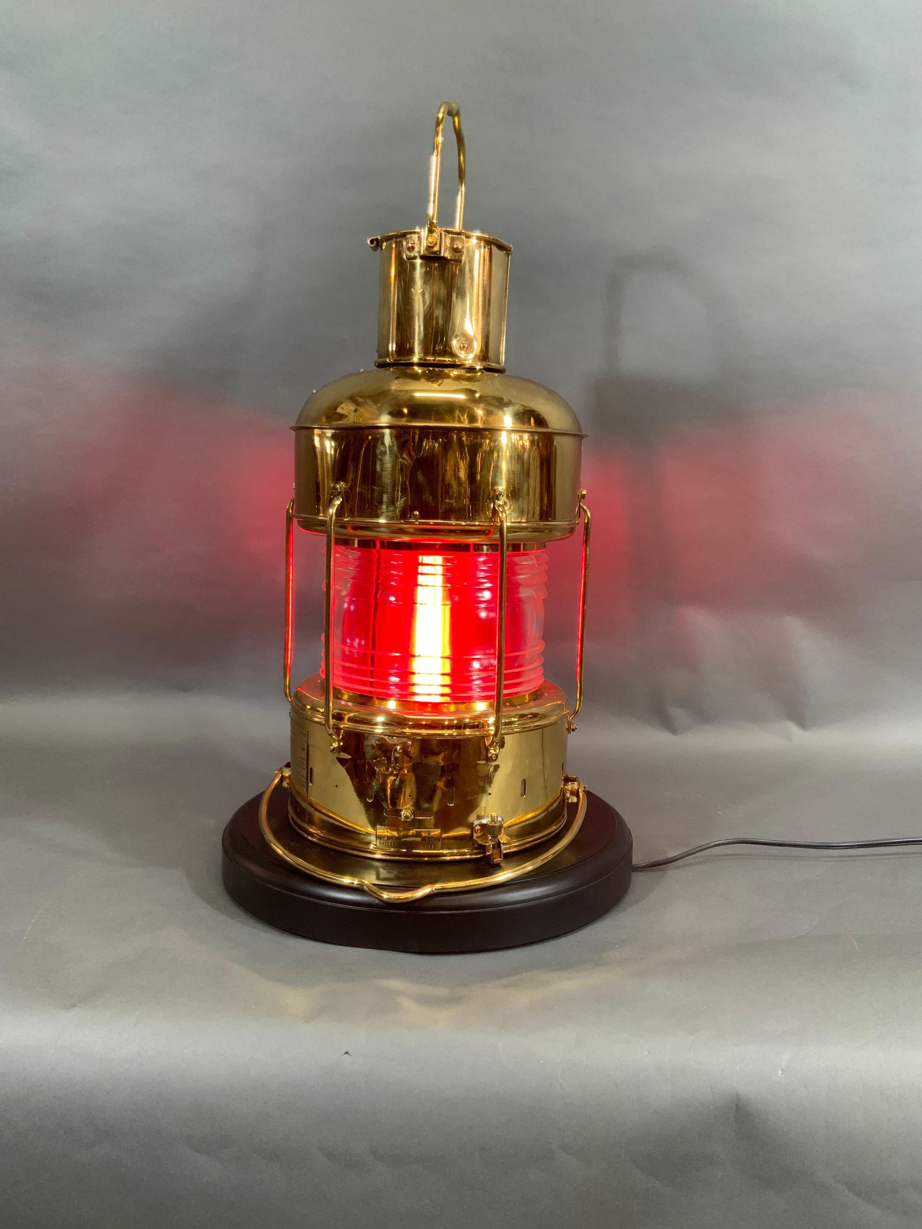Solid brass ship's anchor lantern with glass Fresnel lens, internal removable red filter, hoisting handle, wiring for home use, etc.. This lantern has been meticulously polished and lacquered. Mounted to a thick mahogany base.

Overall dimensions:
