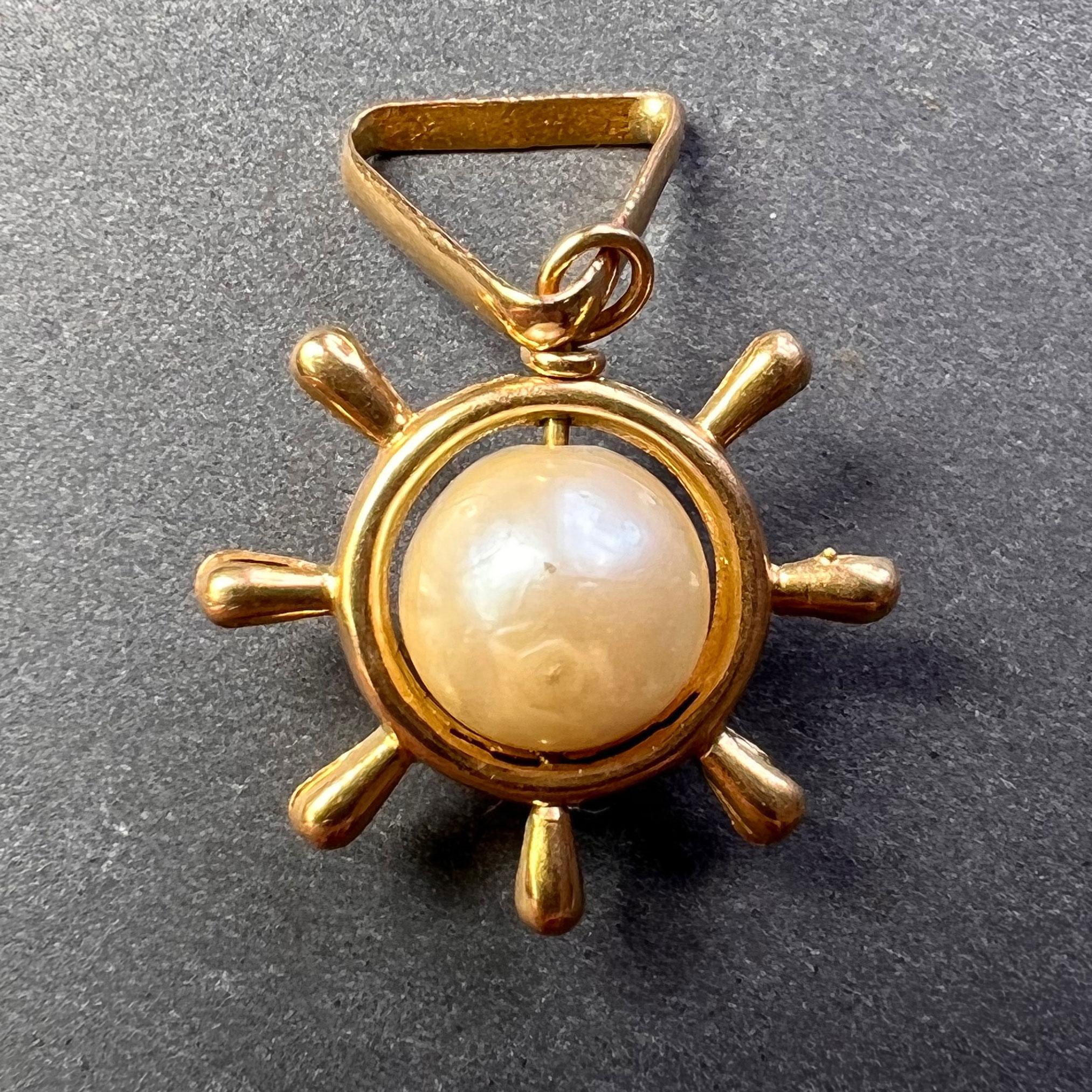 An 18 karat (18K) yellow gold charm pendant designed as a ships steering wheel centering a white cultured pearl. Unmarked but tested as 18 karat gold.
 
Dimensions: 1.7 x 1.7 x 0.75 cm (not including jump ring)
Weight: 1.75 grams
(Chain not included)