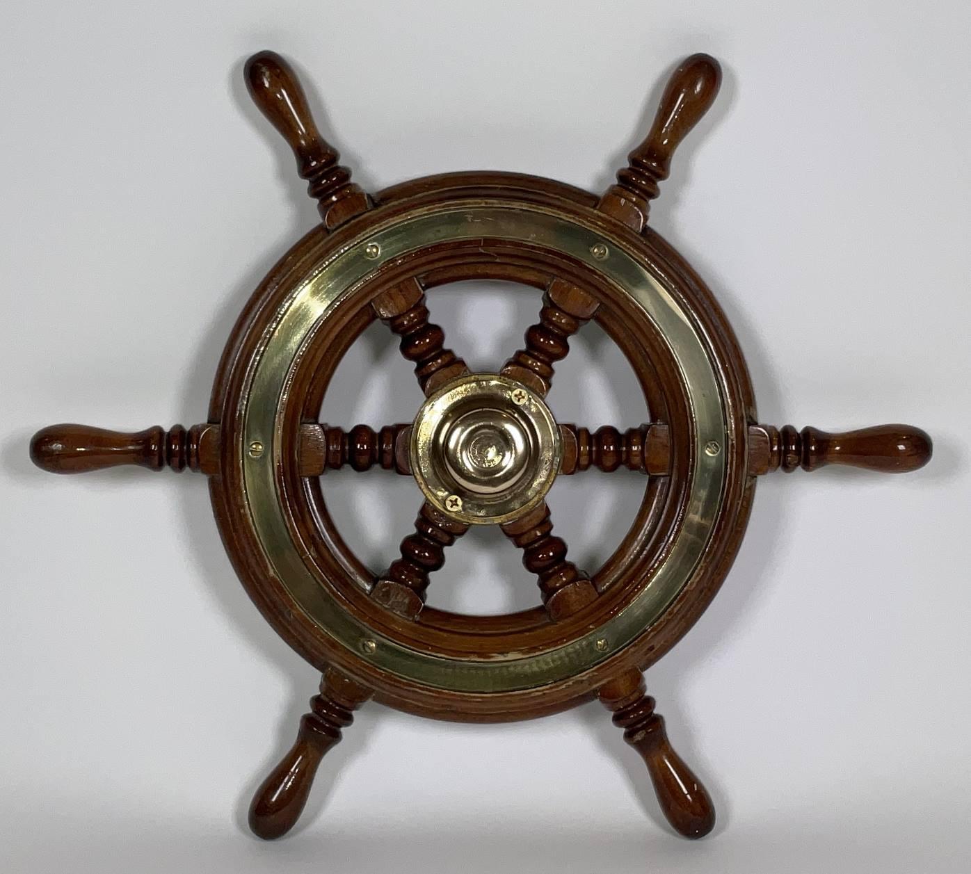 Rueda de barco de seis radios de Simpson Lawrence de Inglaterra. Marco de madera barnizada con incrustaciones de anillos embellecedores de latón y tapa de cubo de latón. La gorra tiene a Simpson Lawrence y el logotipo de su empresa en el cubo. Se