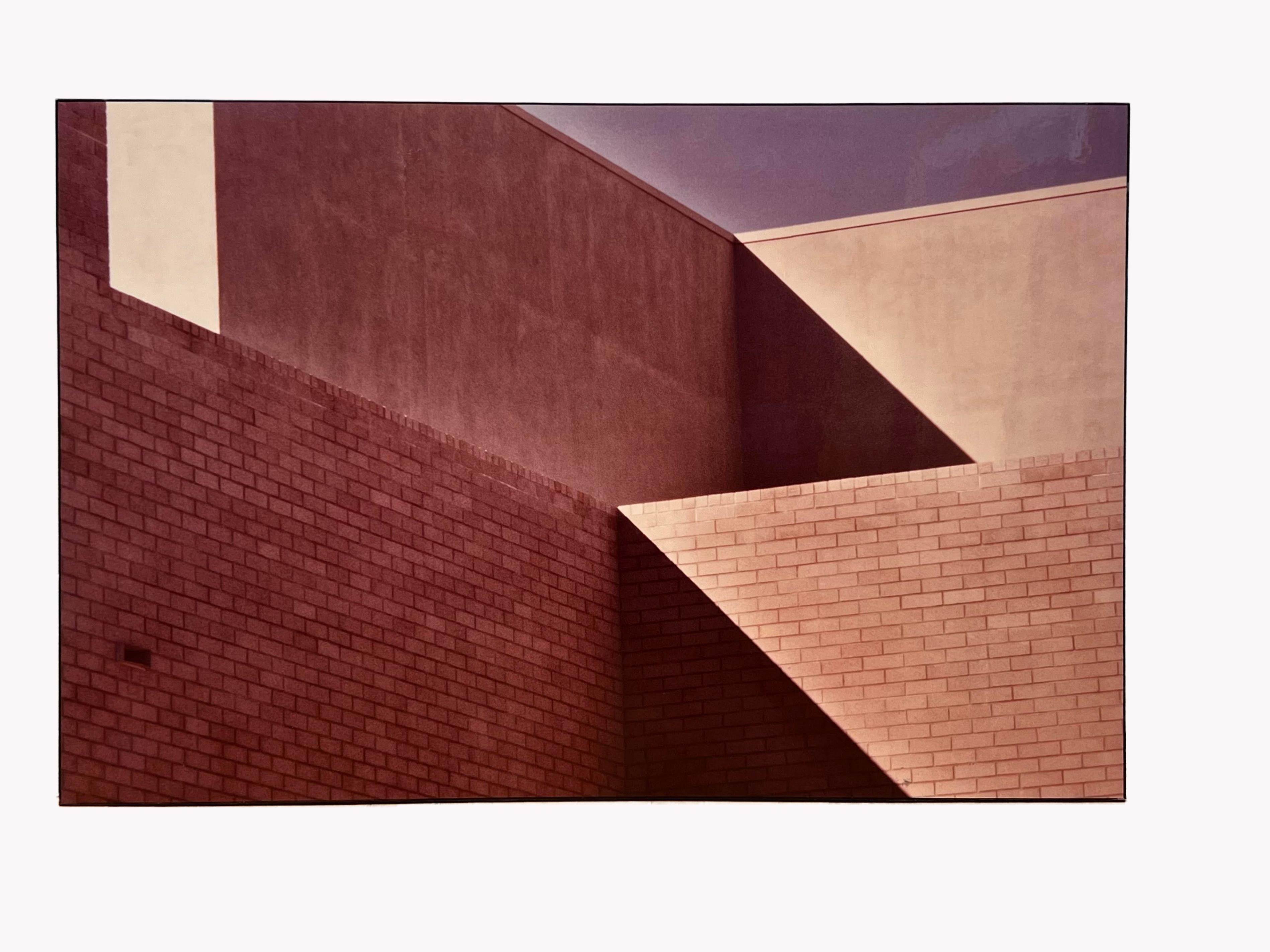 Shirley Bleviss approaches architectural photography as a painter might approach canvas—seeking geometry, light, and rhythm rather than mere documentation. In this photograph, she isolates the junction of brick and stucco walls, their planes sharply
