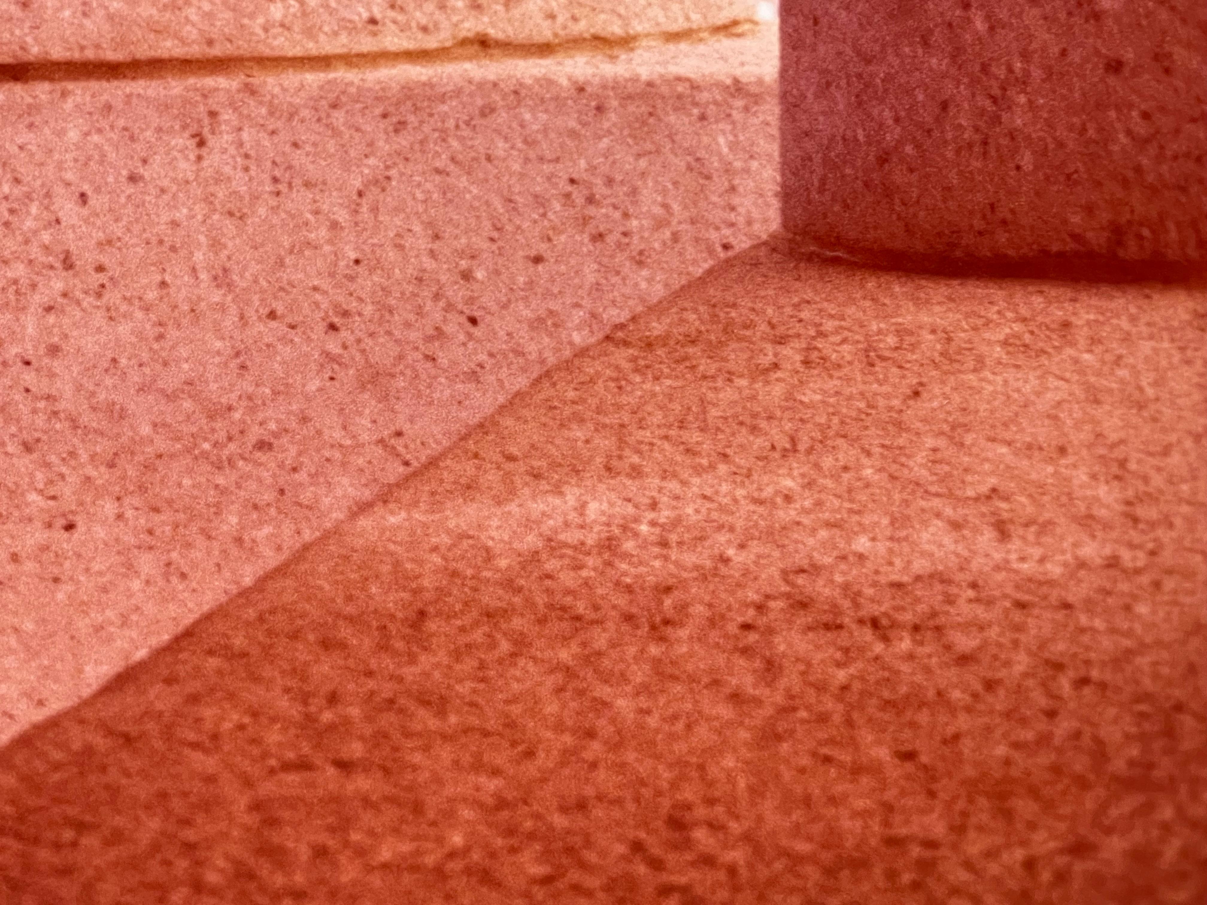 Through a meticulous focus on architectural detail, Shirley Bleviss transforms an ordinary fragment of structure into an interplay of geometry, texture, and light. The image centers on the base of a column, rendered in warm tonal hues, its curved