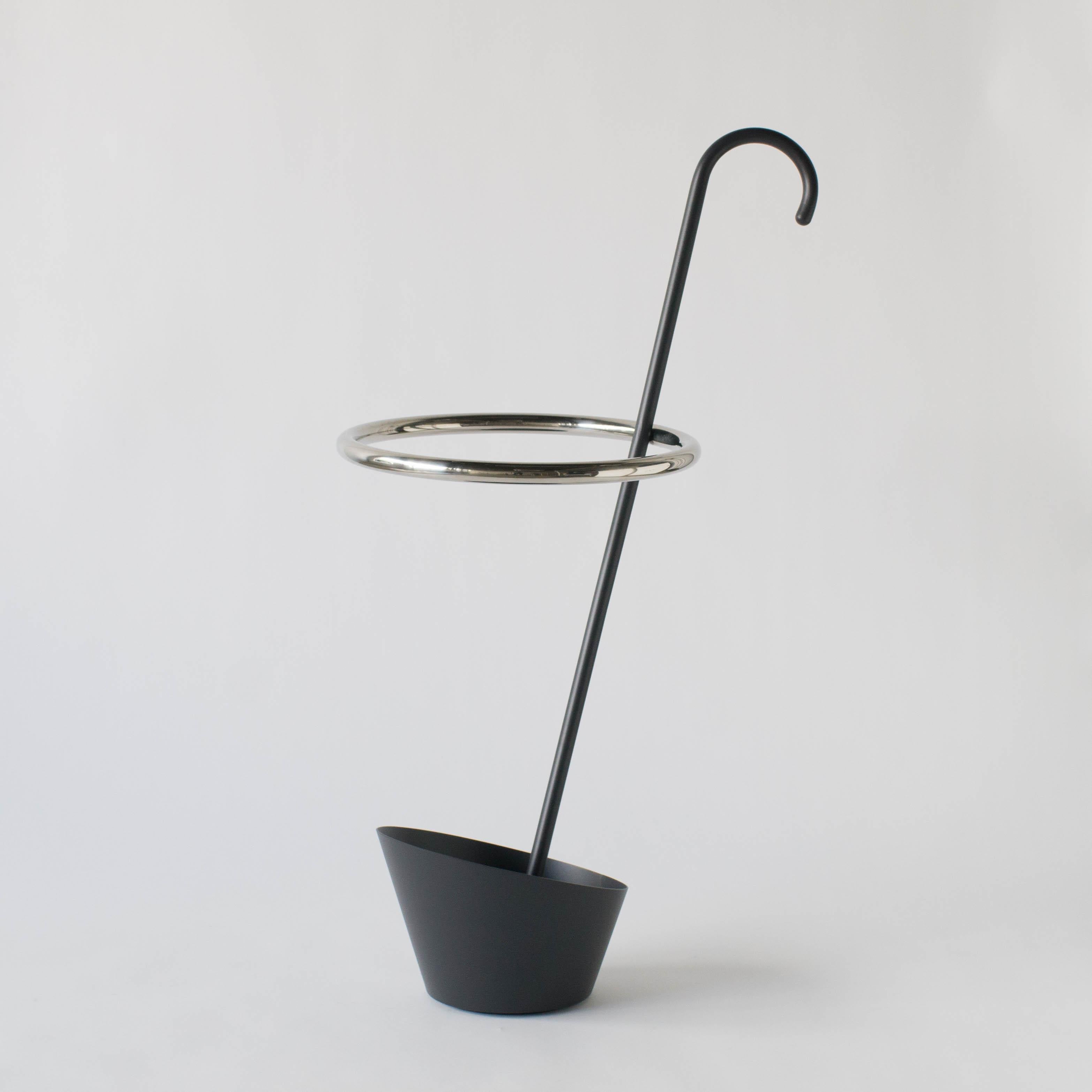 Shiro Kuramata umbrella stand. Made by stainless steel. Base and bar are black painted stainless steel. New piece.
Designed by Shiro Kuramata in the 80s. He designed this umbrella stand with his humor. While umbrellas are put in it, black curved