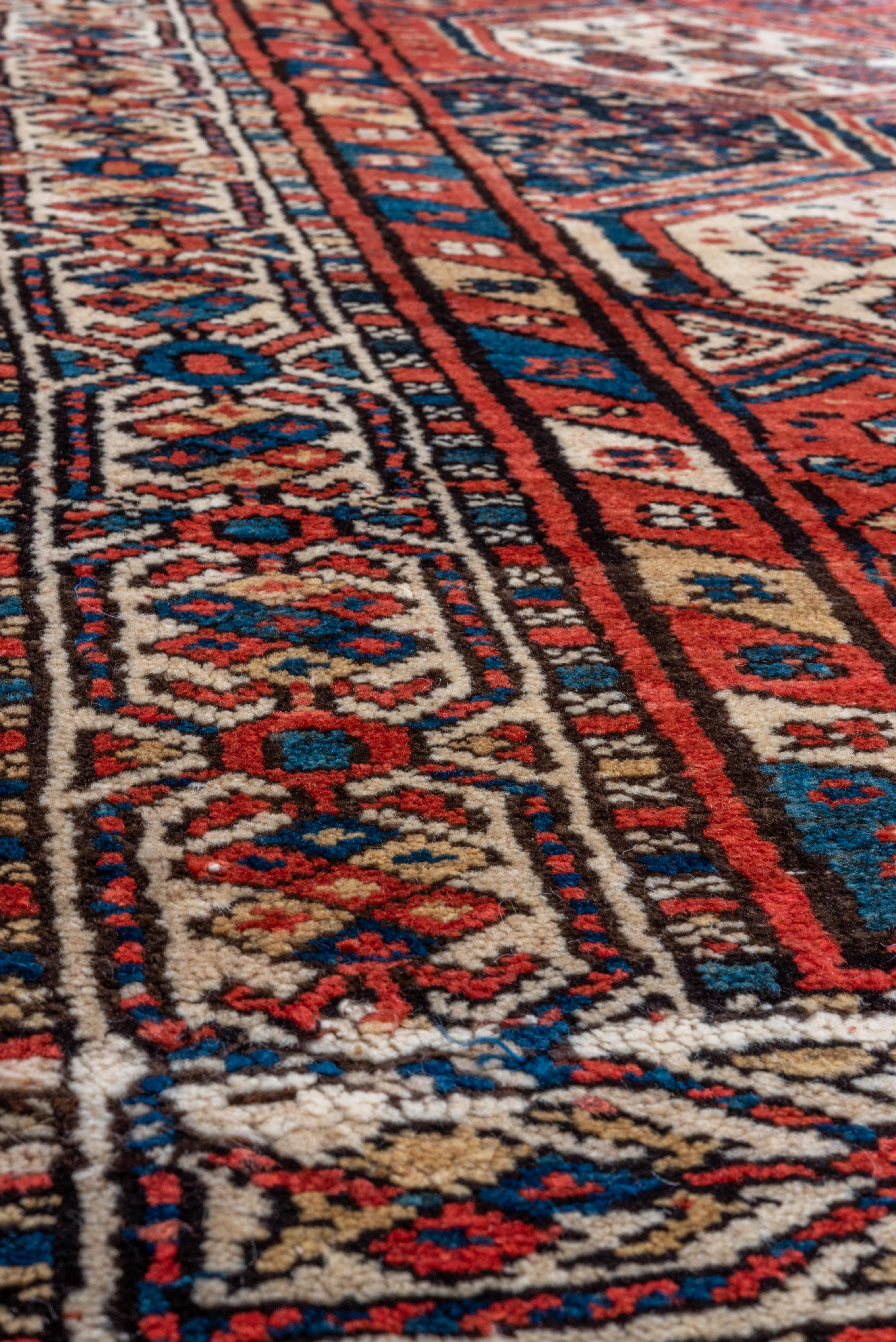 This antique Shirvan runner showcases the hallmarks of Caucasian tribal weaving with its dynamic hexagonal medallions and densely packed field. The bold crimson ground is intricately patterned with ivory and navy medallions, filled with stylized