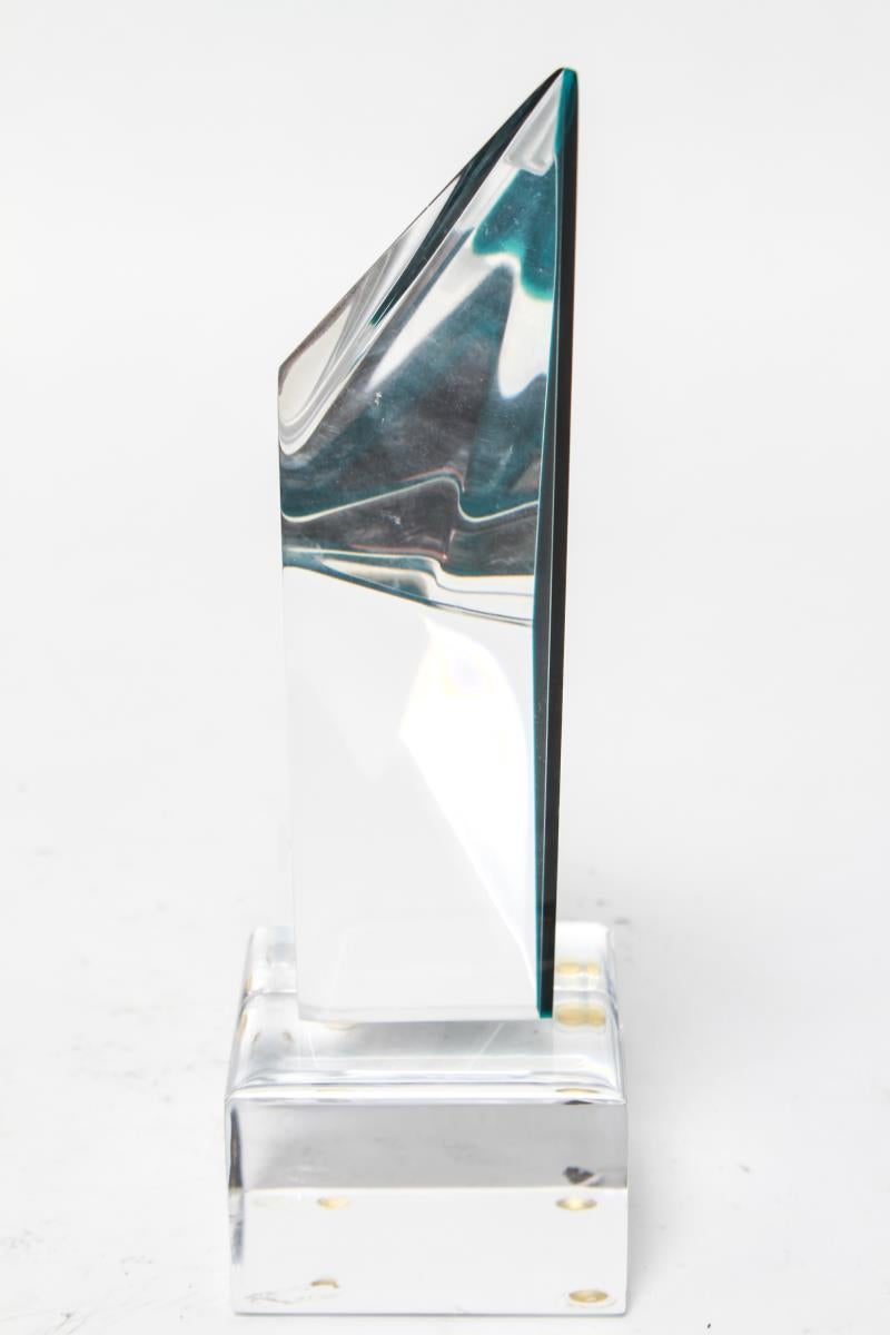 Abstract modern sculpture by Israeli artist Shlomi Haziza in shape of an acrylic faceted chevron in changing shades of blue, turquoise and green, mounted on a clear acrylic base. The piece has a Haziza label on one of the sides of the acrylic base