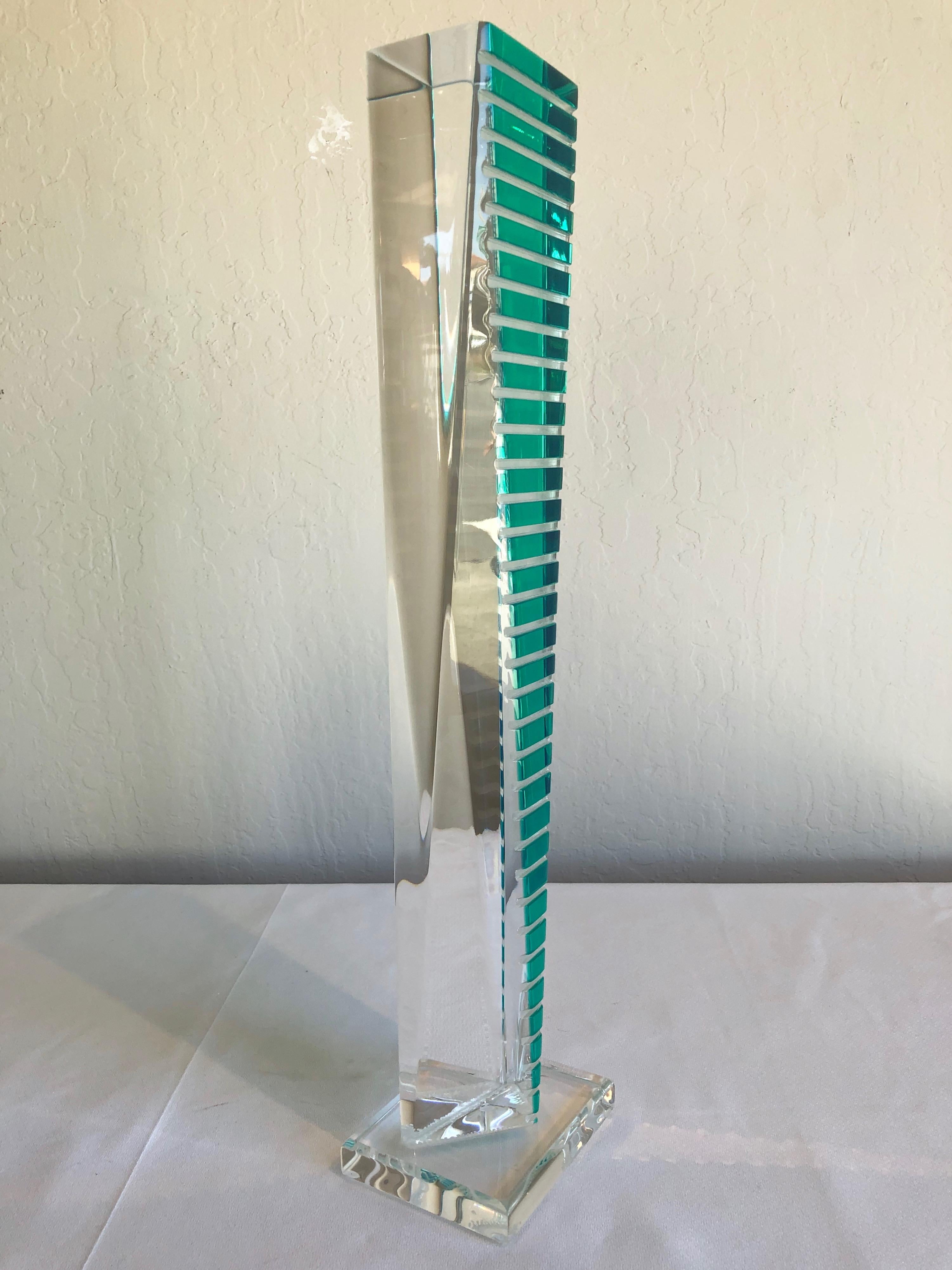 Architectural skyscraper-like form of faceted crystal clear solid lucite transitions from a triangular bottom to a rectangular top. Accented on one side by thirty-five stepped bars of translucent turquoise. Exacting geometry results in dynamically
