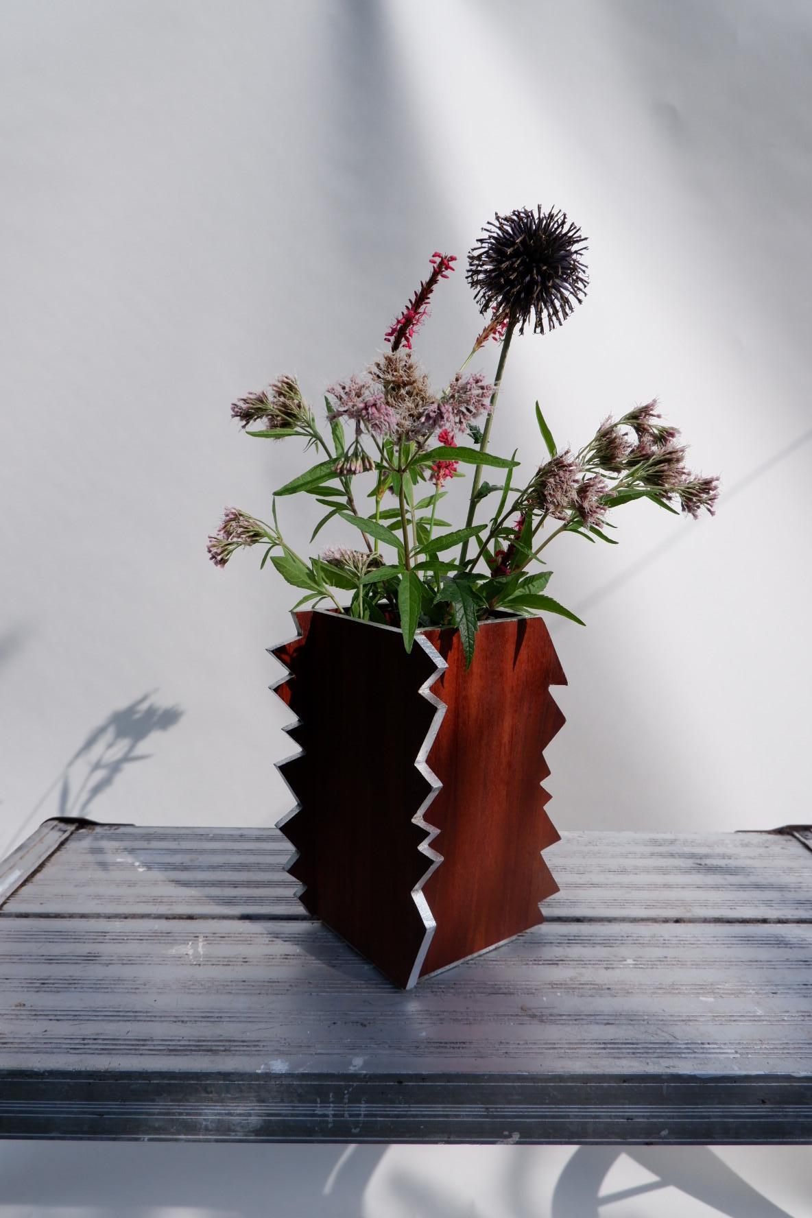 Il Vaso Sconvolgente. Un look moderno e deciso in contrasto con le tue composizioni organiche. Progettato per aggiungere un tocco di drammaticità al piano del tuo tavolo.

Realizzato in Sapele e bordi dorati a olio con alluminio. Ogni vaso viene