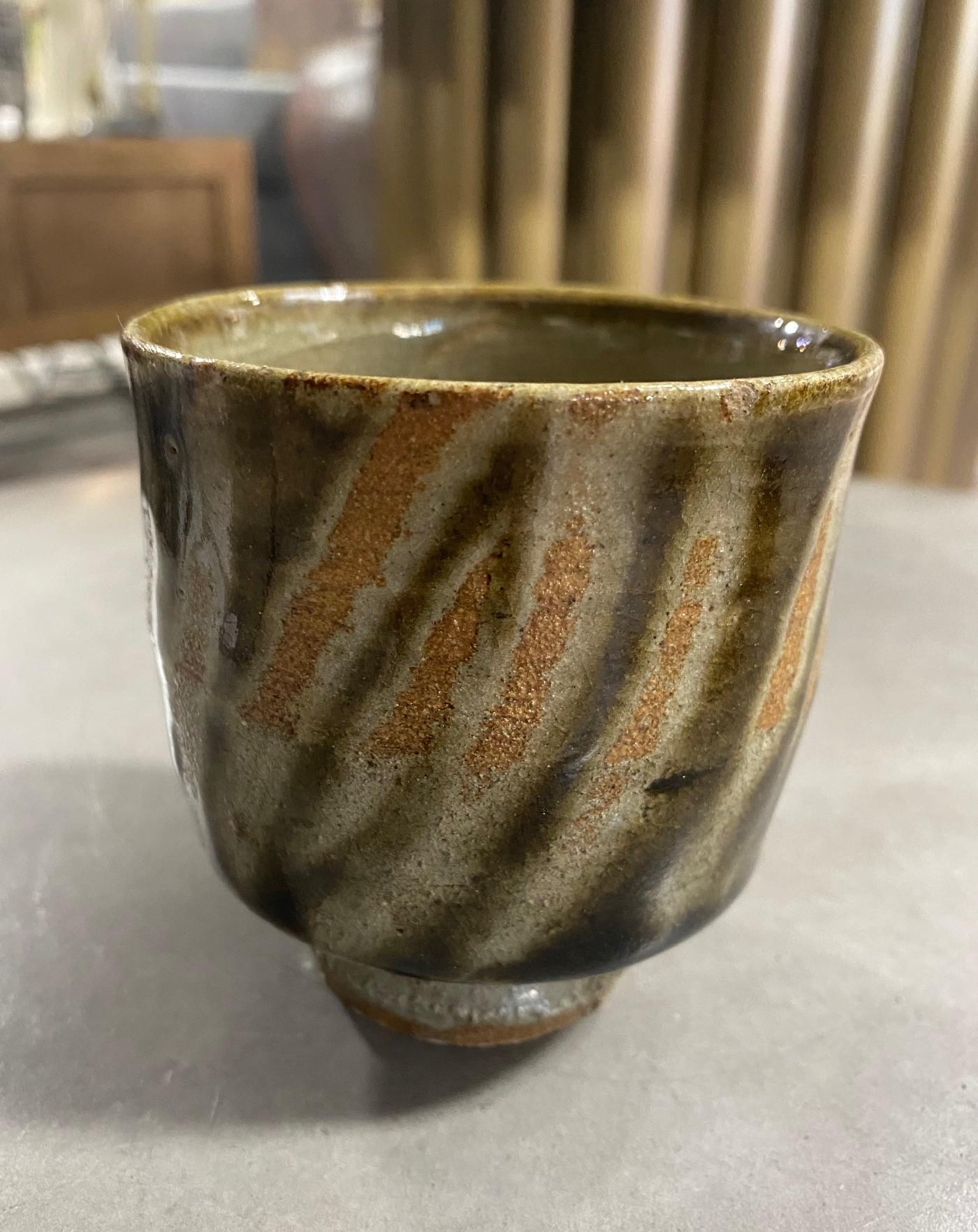 An exquisite, beautifully glazed yunomi tea cup by master Japanese potter Shoji Hamada featuring Hamada's famous diagonal finger wipe technique and a glossy dark celadon Oribe rice ash glaze which is accentuated by the underlying iron-laden clay