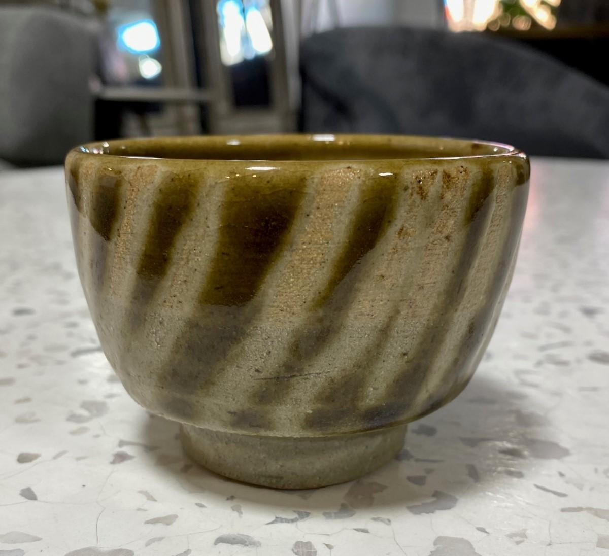 An exquisite, beautifully glazed Yunomi tea cup by master Japanese potter Shoji Hamada featuring Hamada's famous diagonal finger wipe (swipe) technique and a glossy dark celadon Oribe rice ash glaze which is accentuated by the underlying iron-laden