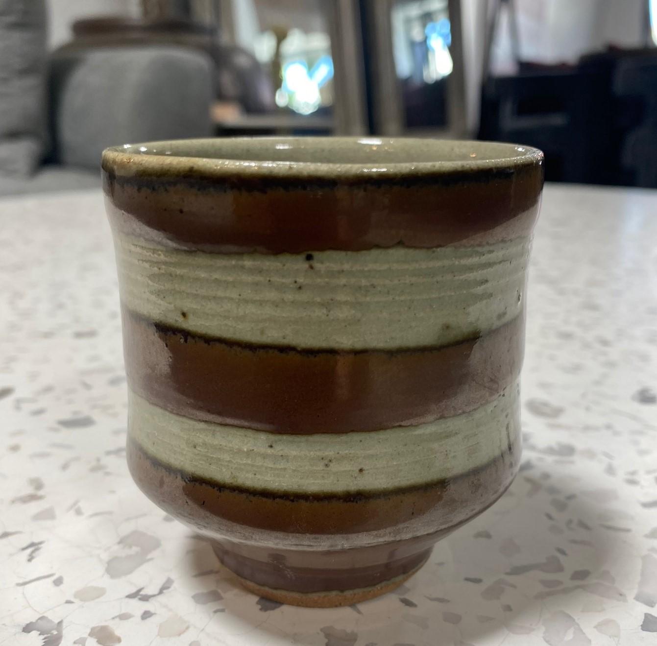 An exquisite, beautifully crafted, and wonderfully designed Yunomi teacup by master Japanese potter Shoji Hamada featuring his wax-resistant technique and highly coveted thick rich Kaki glaze over Mashiko stoneware pottery in a circular striped