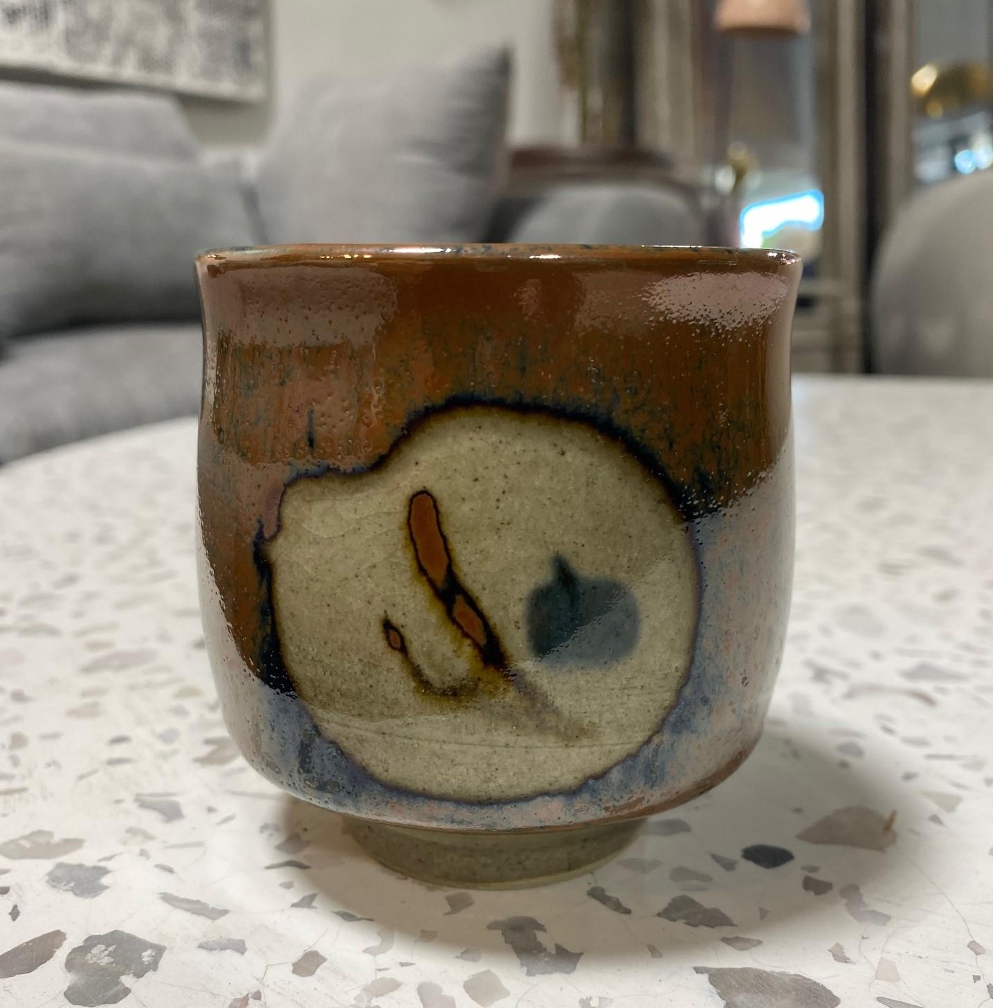 Eine exquisite, wunderschön gearbeitete und wunderbar gestaltete Yunomi-Tasse des japanischen Töpfermeisters Shoji Hamada mit seiner wachsresistenten Technik und der begehrten reichen Kaki-Glasur auf Mashiko-Steinzeugkeramik. Ein einzigartiges Werk.