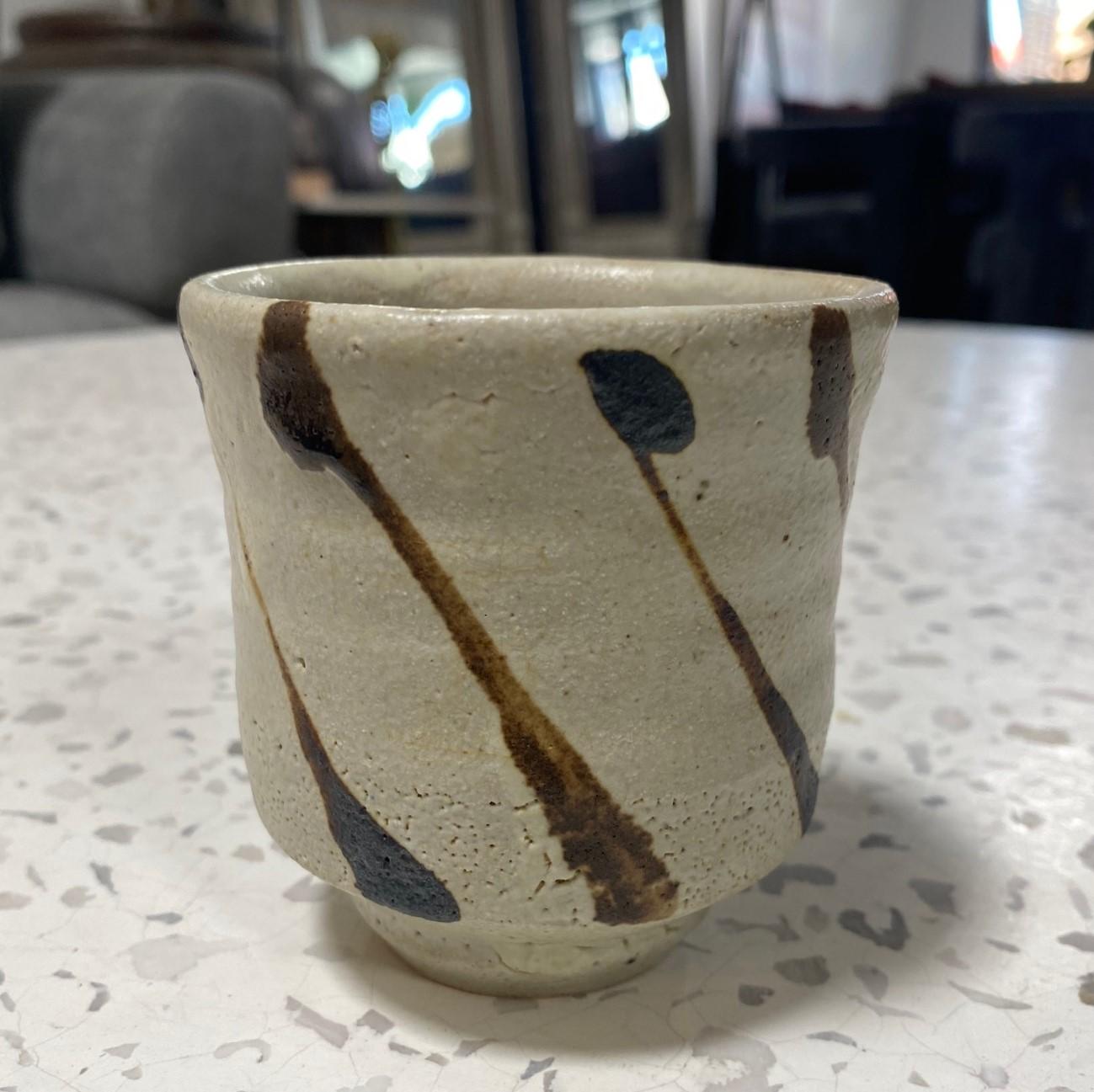 Une exquise tasse à thé Yunomi rayée, magnifiquement fabriquée et conçue par le maître potier japonais Shoji Hamada, avec son émail nuka sur la poterie en grès Mashiko et un motif en fer peint à la main. Une œuvre unique. Il est rare de trouver une