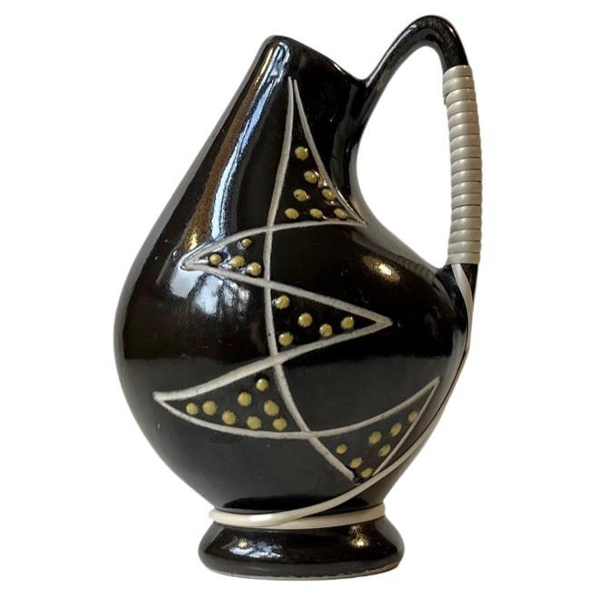 Black ceramic jug vase decorated with a modernistic abstract motif executed in white and yellow glaze. It also features a vinyl/acrylic mesh-handle. Made by Søholm in Denmark, circa 1950-55. Measurements: H: 13.5 cm, W/D: 8/9 cm.