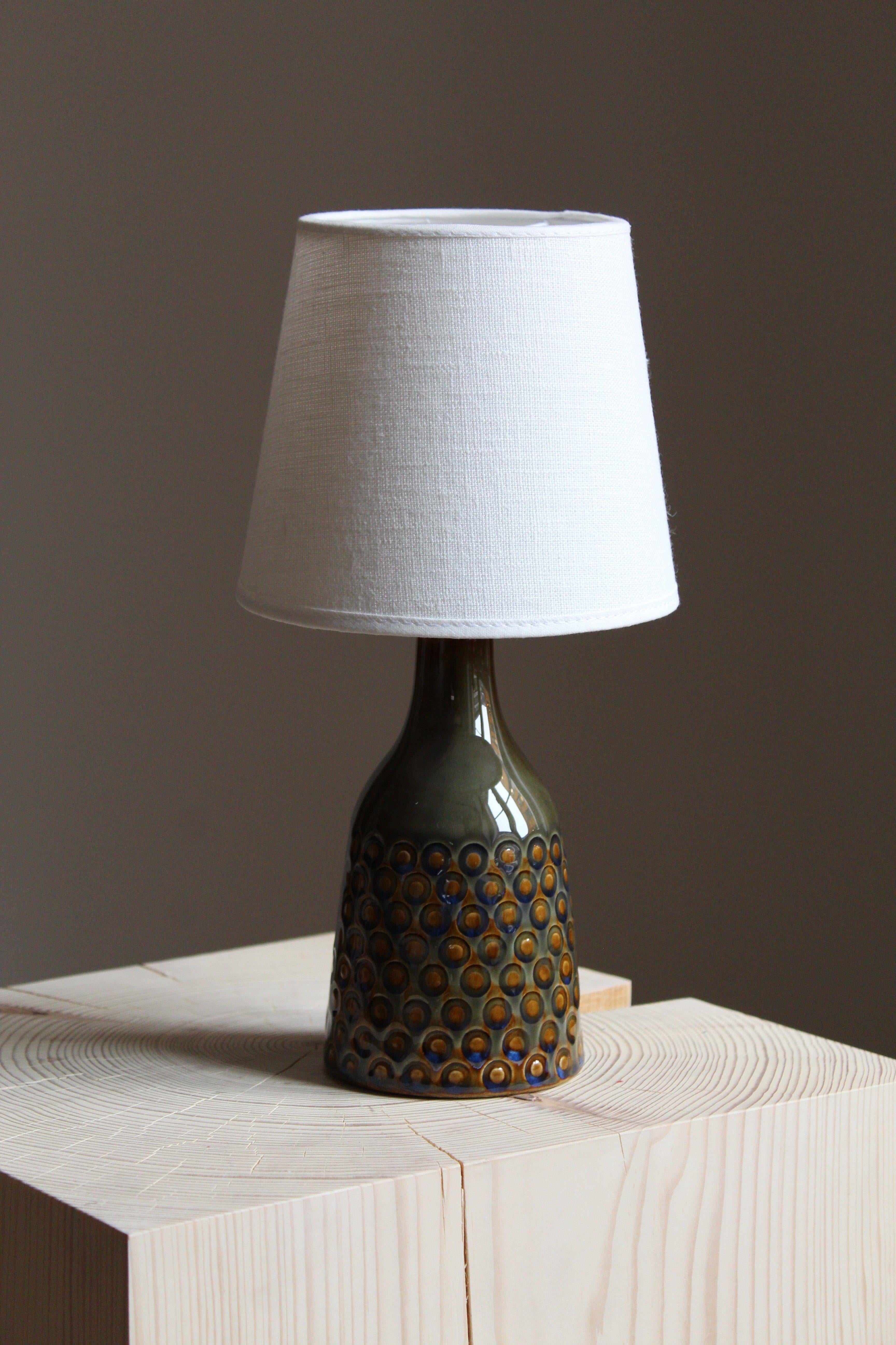 A small table lamp produced by Søholm Keramik, located on the island of Bornholm in Denmark. Features a highly artistic green / blue glaze. 

Lampshade not included. Stated dimensions measured with illustrated model lampshade attached.

   