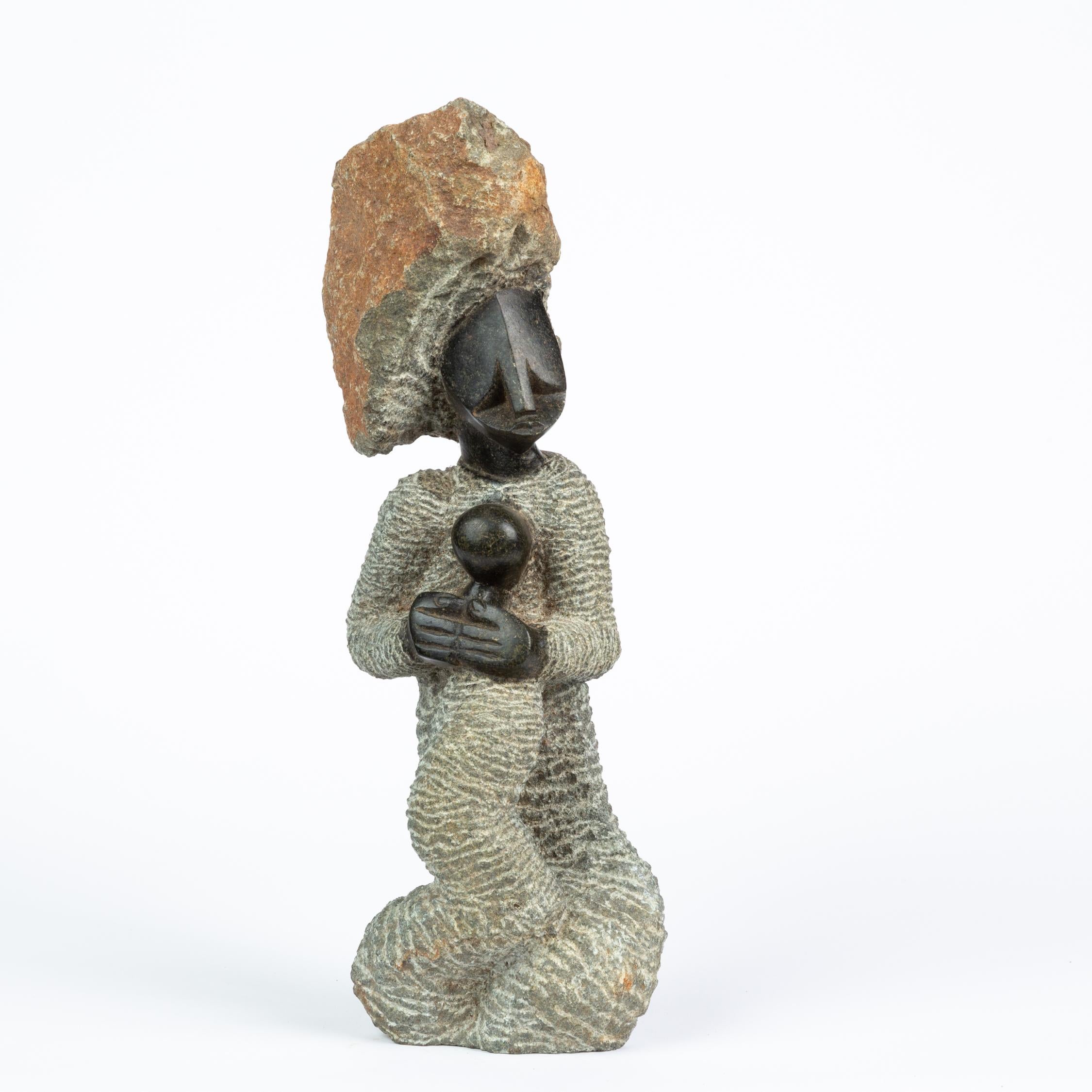 A hand carved statuette of a mother and child in the Shona style of Zimbabwe. The sculpture, carved from black springstone, uses areas of high polish to show the heads and hands of the figures, and works with the natural texture of the stone to