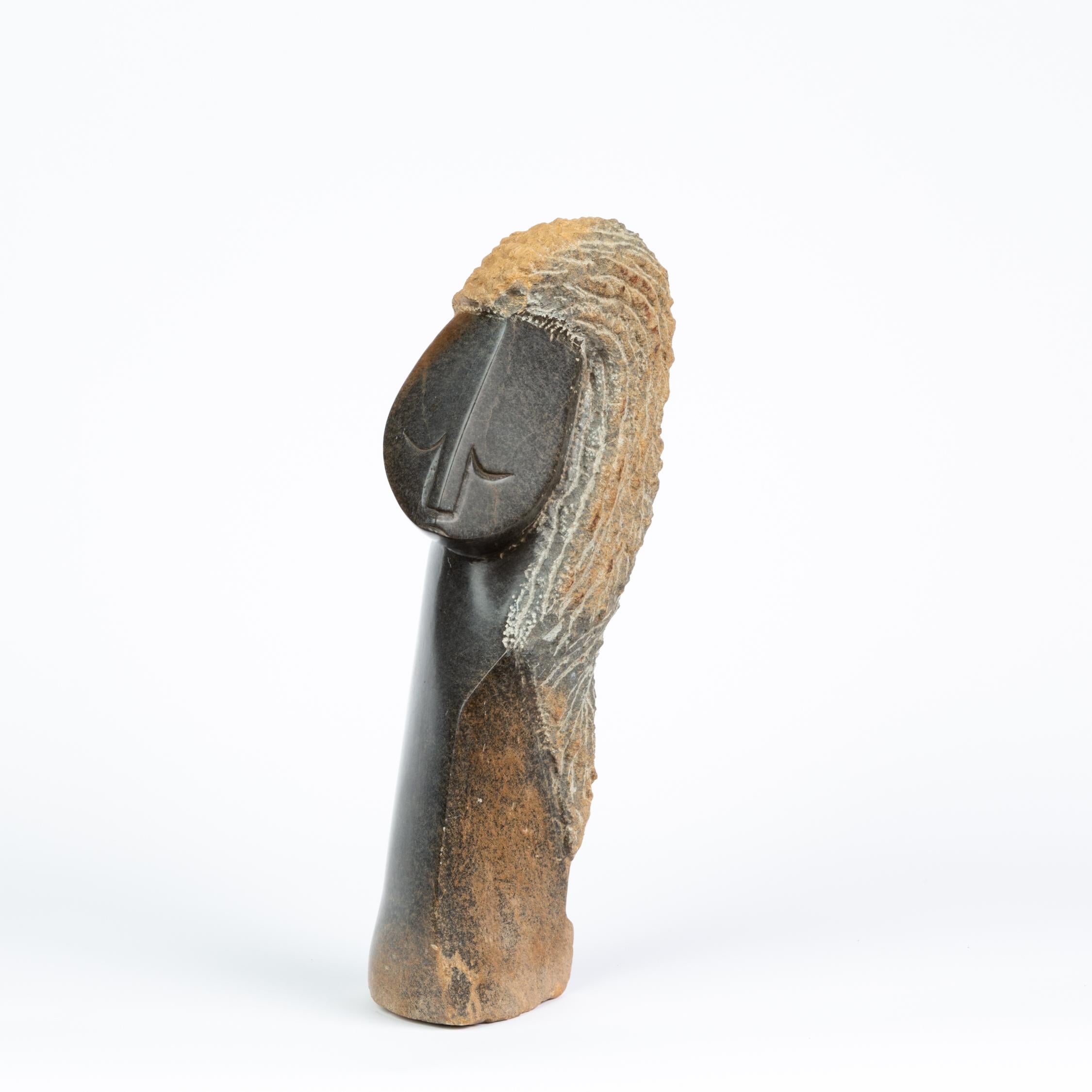 A hand carved sculpture of a human figure in the Shona style of Zimbabwe. The sculpture, carved from black springstone, uses areas of high polish to reveal an angular head and peaceful visage with closed eyes, while working with the natural texture
