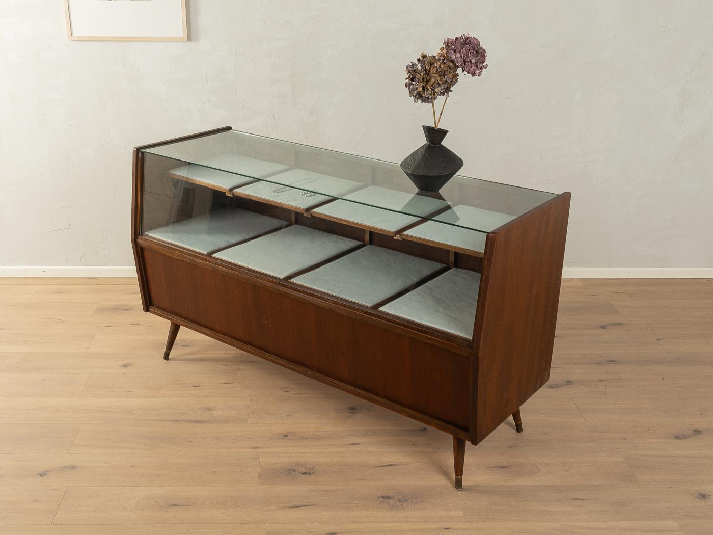 Wonderful shop counter from the 1950s. Corpus in walnut veneer with eight hinged doors, eight pull-out shelves covered with high-quality fabric in light grey and slanted feet with brass caps.

Quality Features:
very good workmanship
high-quality