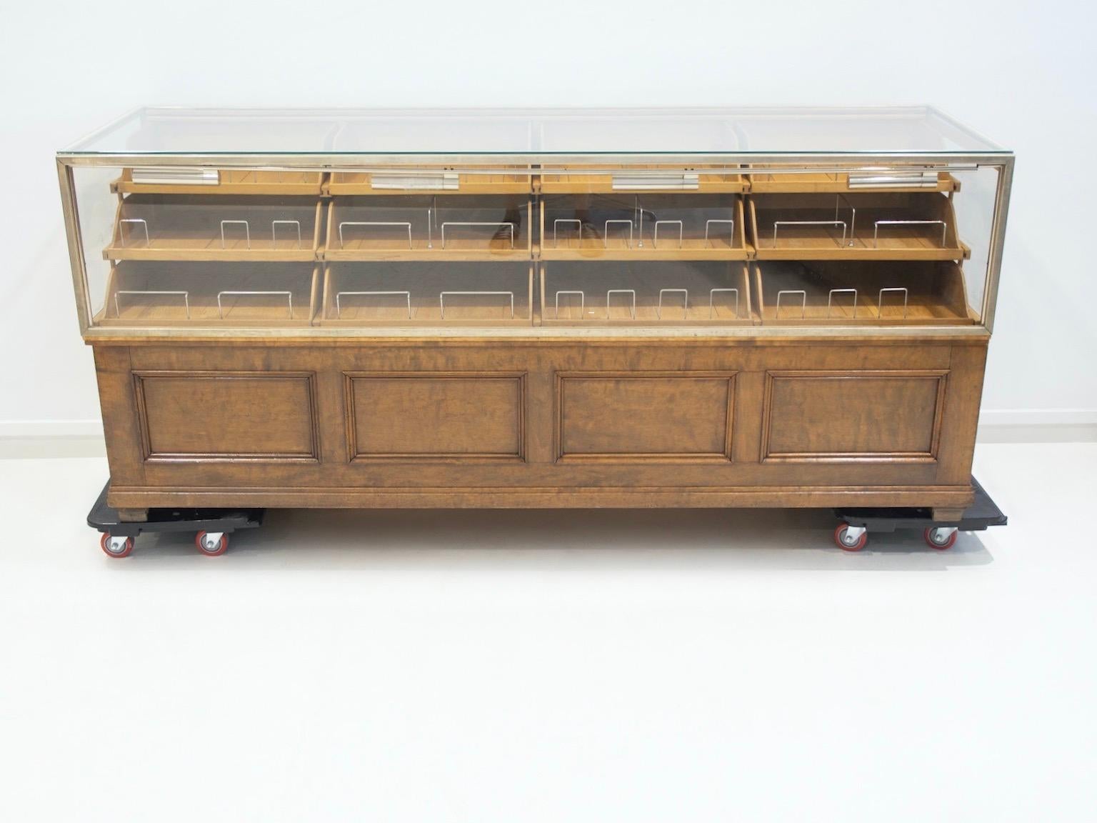 Two-part merchant haberdashery counter made of birch and oak. Glass upper part with interior compartment of ten display drawers and mounting for lighting. Bottom part with ten larger drawers. Aluminum drawer pulls, brass frame and details. 
One