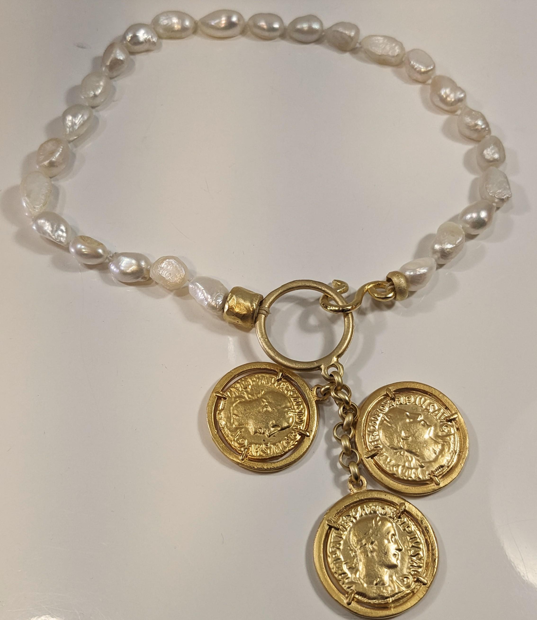  Short Necklace of White River Pearls with Central Hoop and Trio of Coins
 It has a central S-shaped closure. All in 18 karat matte gold
Neck measurement  42cm (16,53 inches)
Coin chain length  9 cm (3,54 inches)


Pradera Fashion Division  is