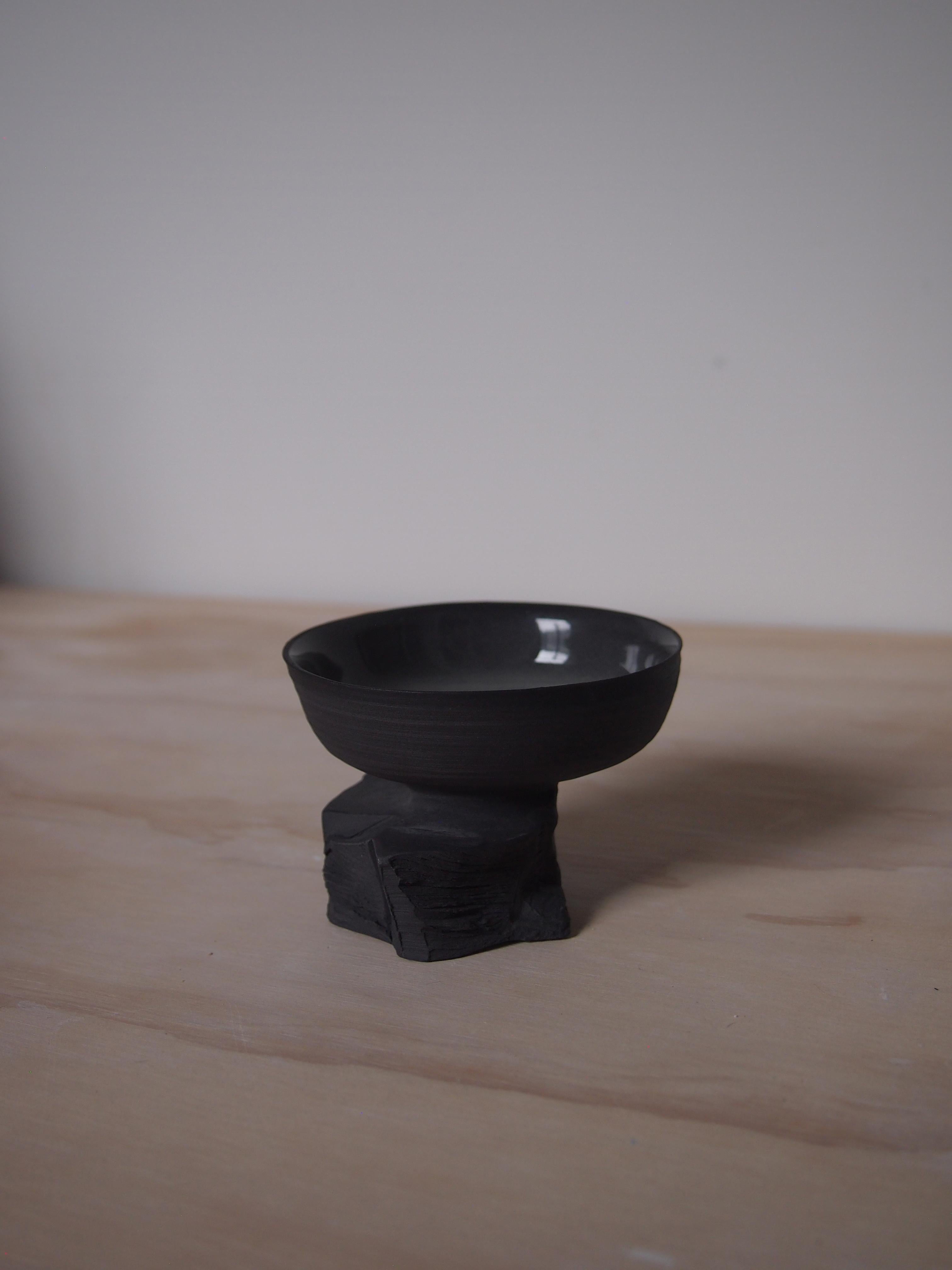 Short Quarry Cup by Liyang Zhang
One Of A Kind.
Dimensions: D 8 x W 8 x H 6 cm.
Materials: Black porcelain. 

Made with single peice of black porcelain. The top is made on the wheel and bottom is made by tearing and chiselling.  The form reveals