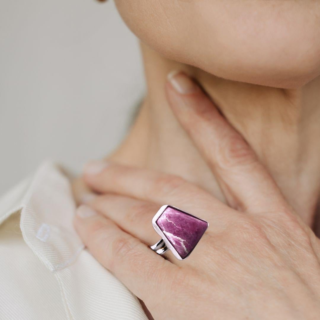 This beautiful and unique ring is sure to be a treasured piece for years to come. Crafted from sterling silver and featuring a trapezoid frame, this ring is set with an incredibly vivid magenta Sugilite gemstone. Though Sugilite is typically found