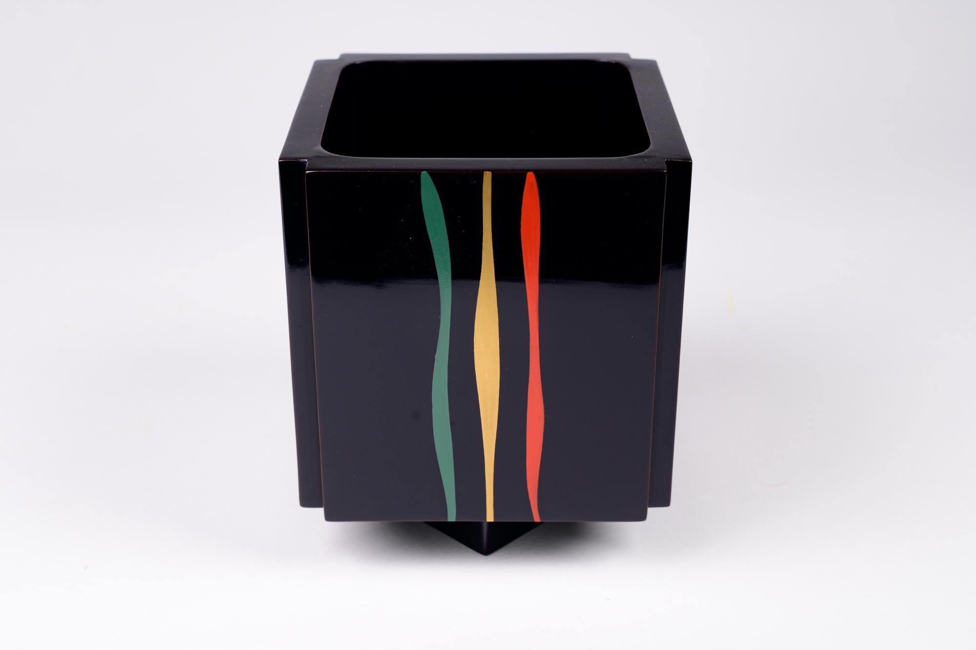 Der Künstler nennt dieses Gefäß in der Kalligraphie auf der Schachtel einen Blumenkorb. Schwarzer Lackbehälter aus der Showa-Periode (1926-1989) in quadratischer Form mit gekerbten Ecken auf einem quadratischen Sockel. Drei farbenfrohe Streifen an
