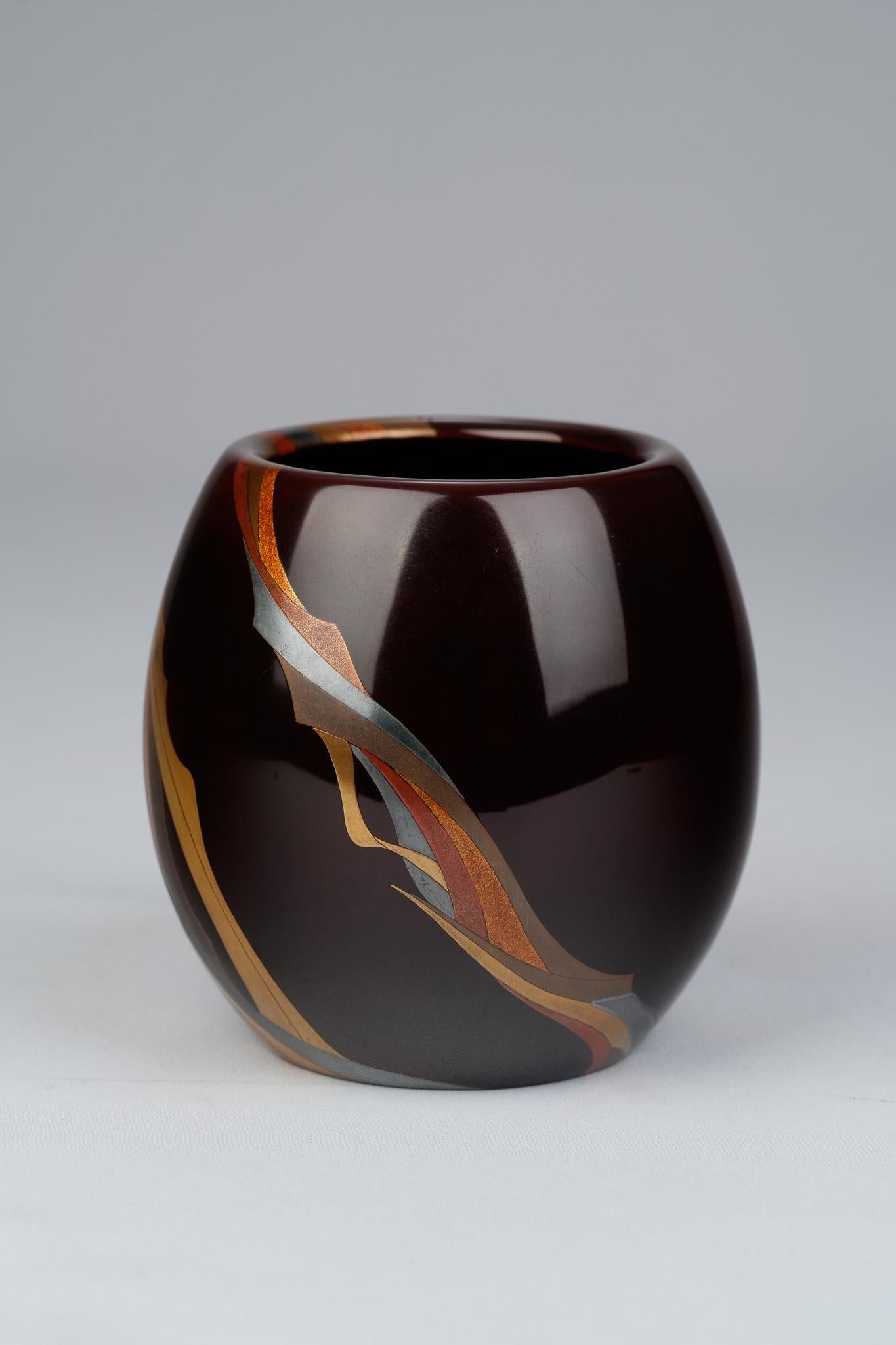 Ce vase en laque de la période Showa, réalisé par Inami Tadashi, présente un mélange élégant d'artisanat traditionnel et d'abstraction moderne. Des bandes d'or, d'argent, de rouge et de tons sourds s'écoulent autour de la surface selon un motif
