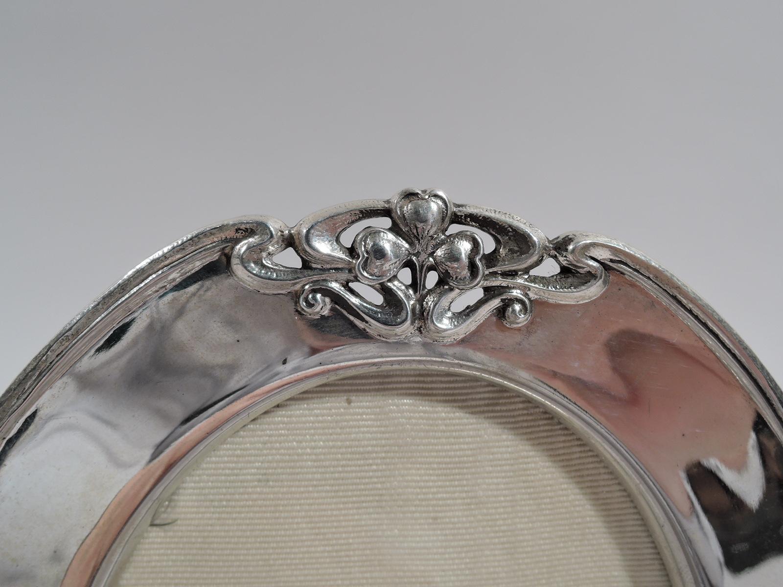 Turn-of-the-century Art Nouveau sterling silver picture frame. Made by Shreve & Co. in San Francisco. Oval window in flat surround; rim molded and interspersed with inset trefoils and whiplash scrolls. With glass, silk lining, and hinged wire