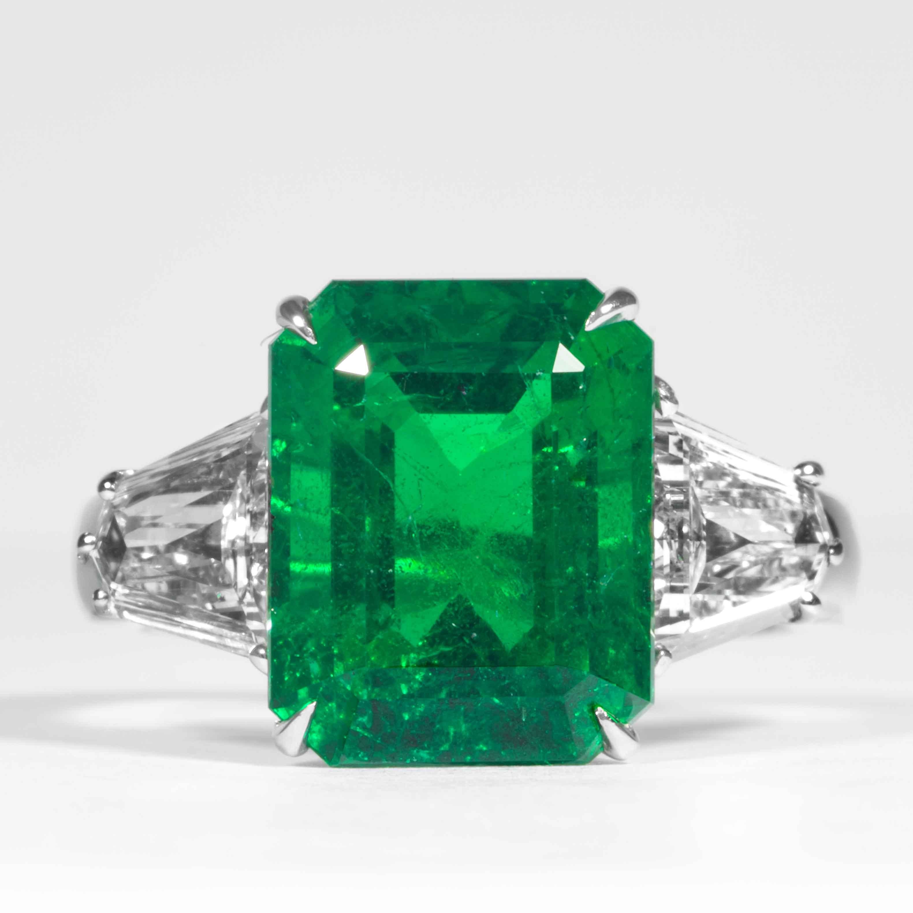 This emerald ring is offered by Shreve, Crump & Low. This green emerald cut emerald is custom set in a handcrafted Shreve, Crump & Low 3-stone platinum ring. This captivating green emerald measures 12.62 x 9.75 x 7.08mm and weighs 6.08 carats.  This