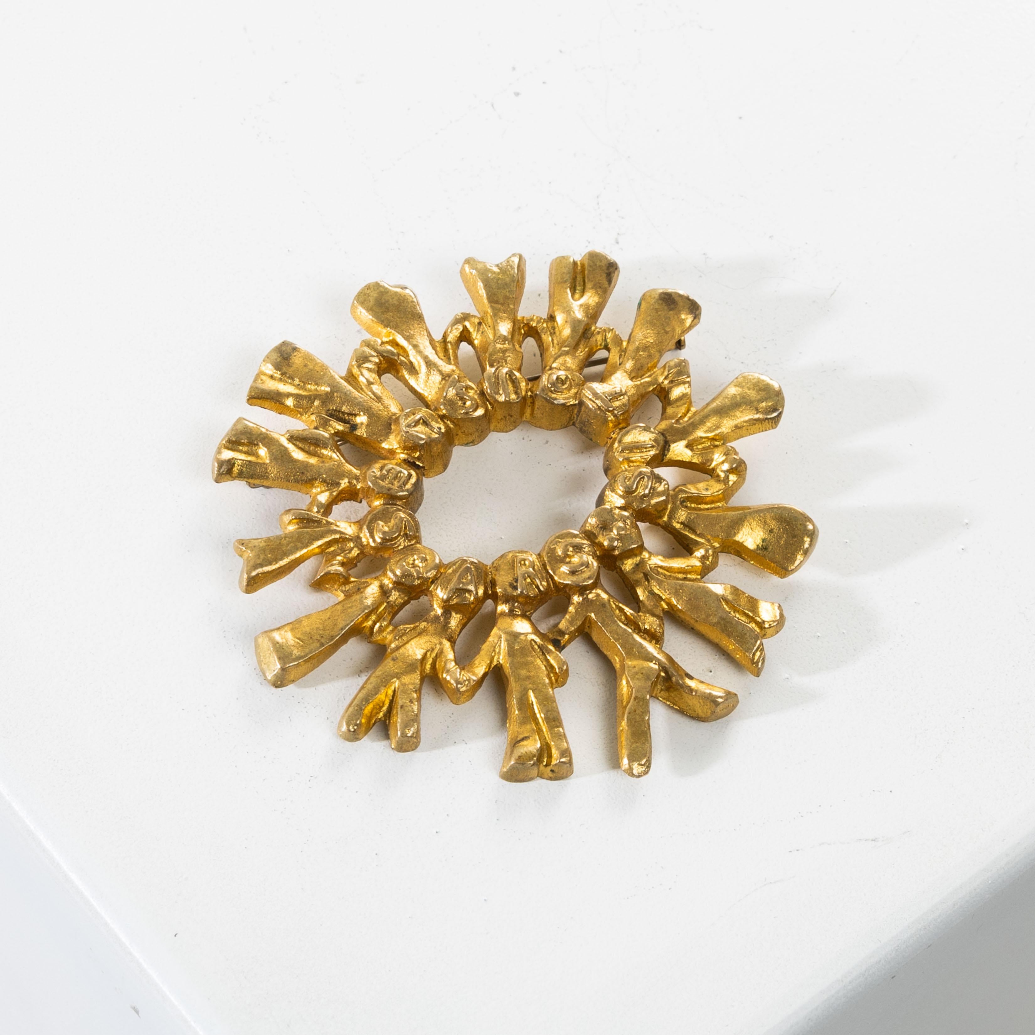 Si tous les gars du monde… (If all the guys in the world…), by Line Vautrin.
Gilt bronze brooch representing a round of 14 children in long dresses.
Based on a stroll (1897) by Paul Fort (1872-1960).
Each child’s head bearing a letter titling the