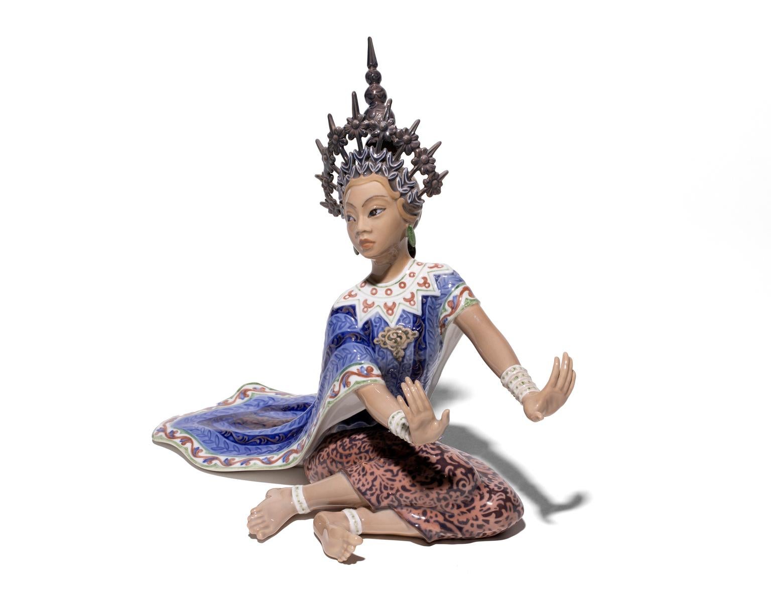 The creator of this piece is Dahl Jensen. The Siamese dancer depicted is no doubt in the Royal Court with her elaborate headdress and elegant robe of indigo blue. The figure has a lovely animation to it as though it is about to stand and continue